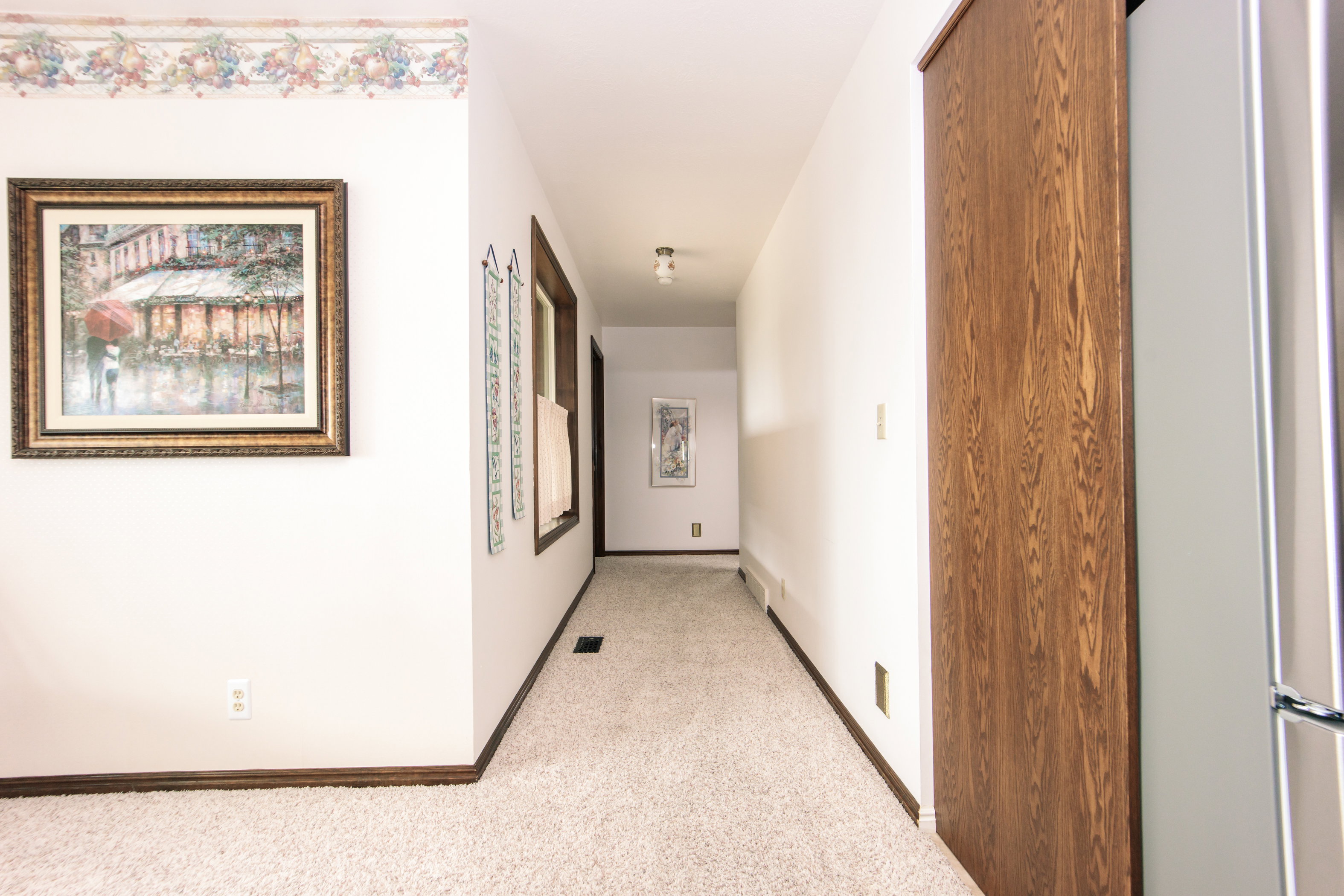 Carpeted hallway featuring white walls, dark wood-finish trim, and a ceiling-mounted light fixture