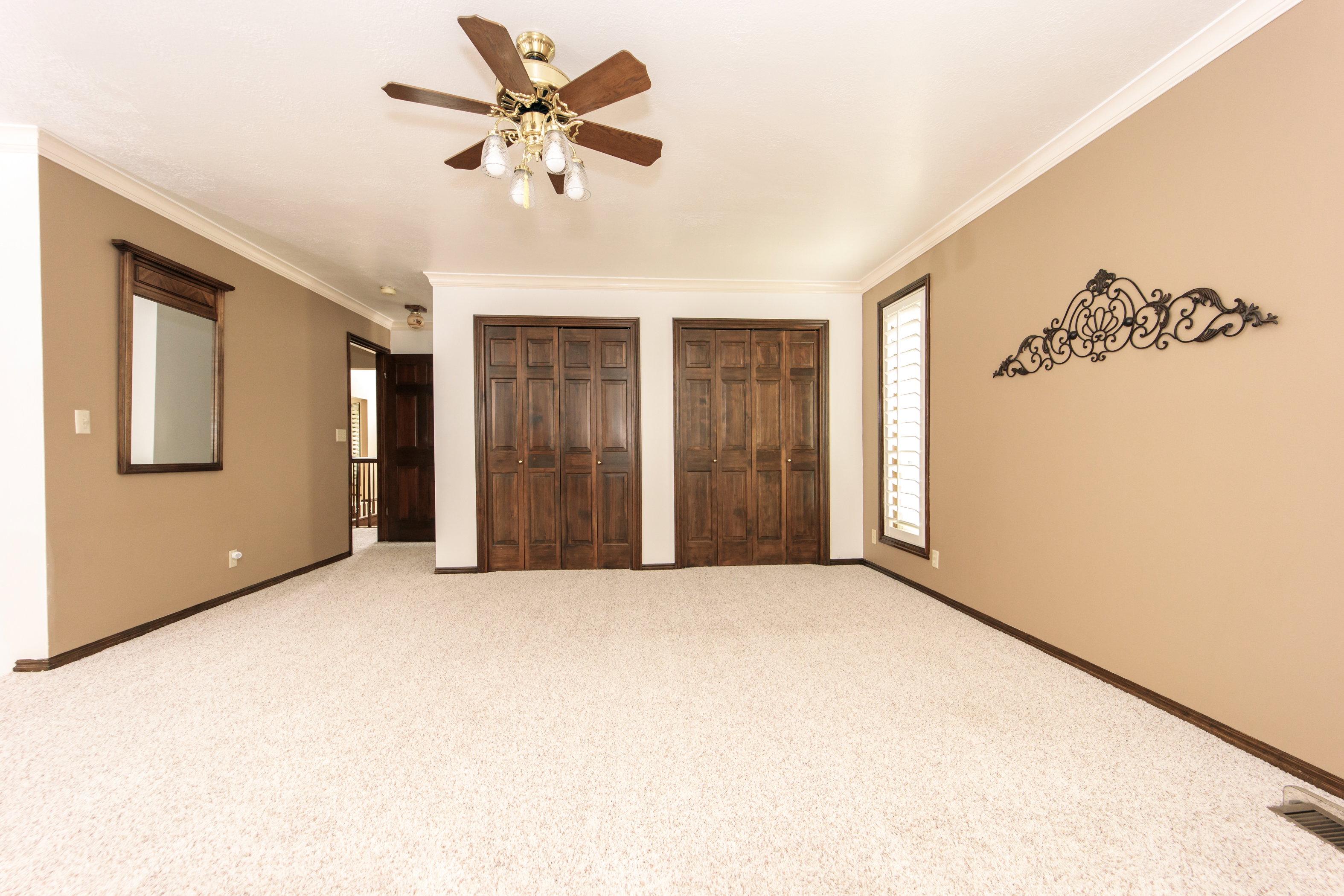 Spacious room with plush carpeting, two sets of bi-fold wood-paneled doors, crown molding, and a ceiling fan with integrated lighting