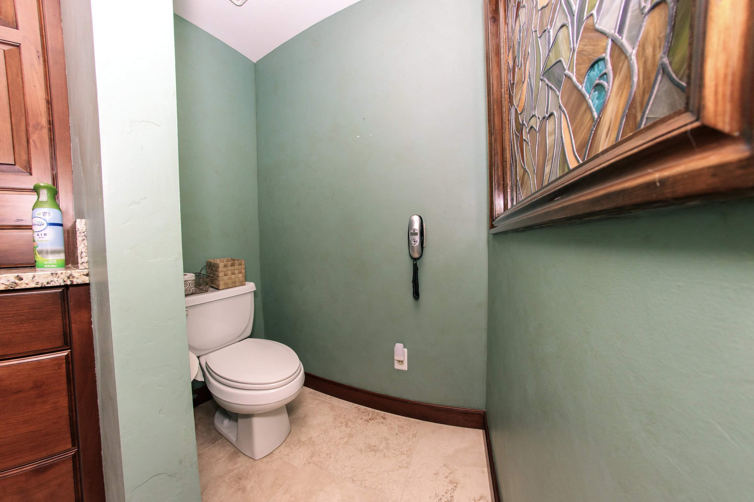 Powder room featuring a white toilet, light-toned floor tiles, and a built-in wood vanity with a granite-style countertop