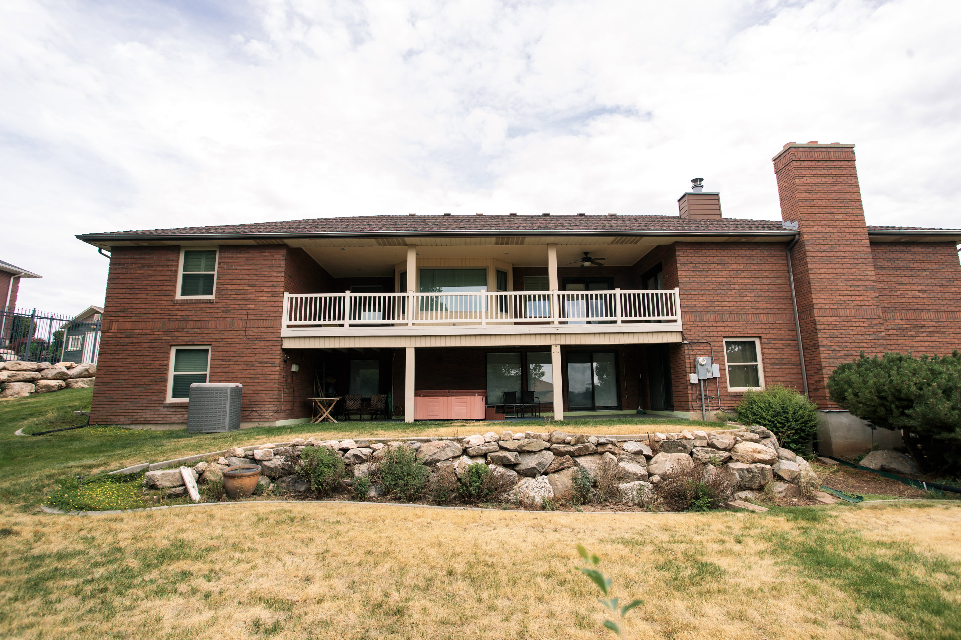 Brick exterior featuring a two-story design with a covered upper-level balcony and a ground-level patio