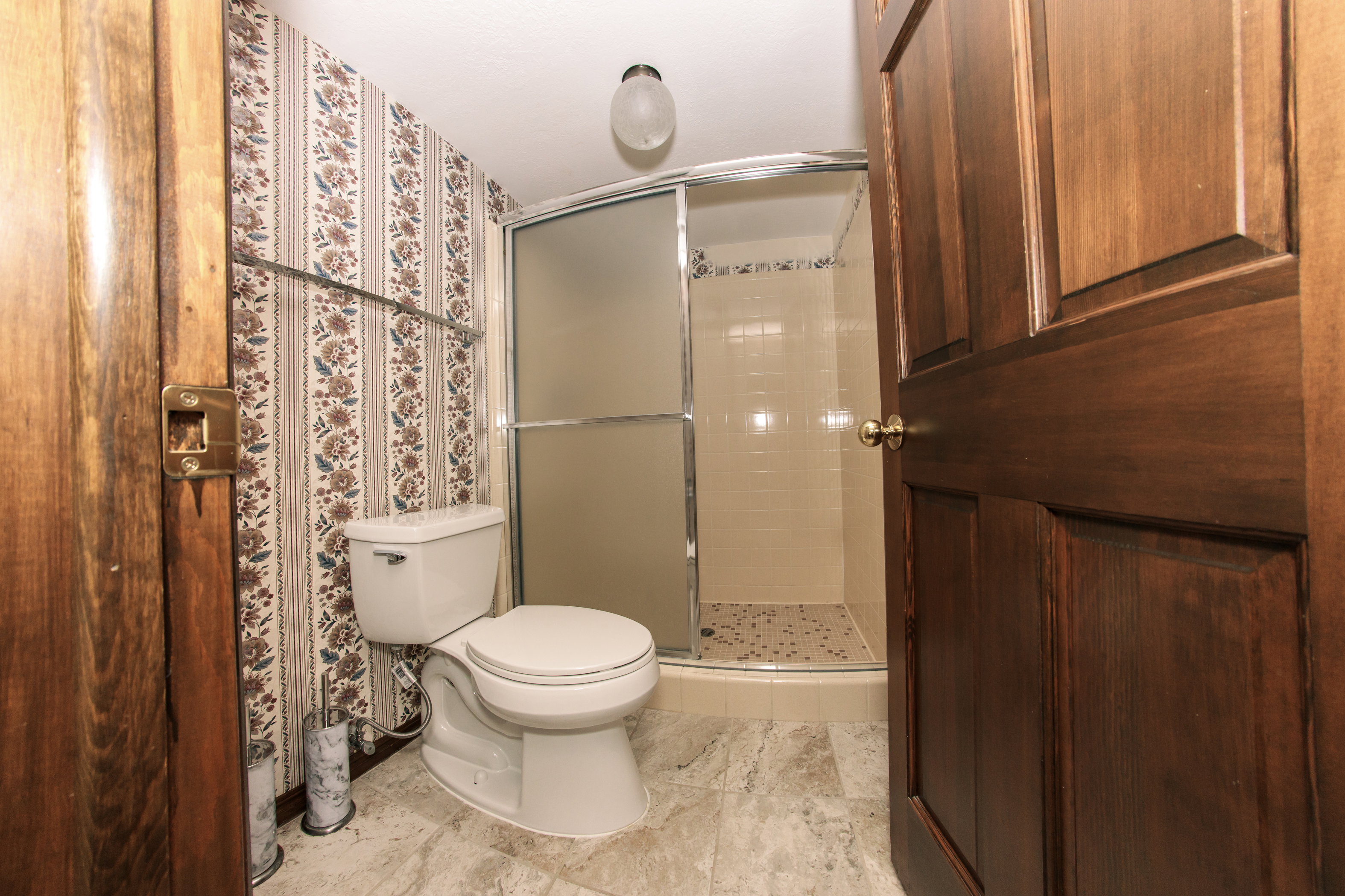Bathroom featuring a white toilet, patterned wallpaper, and a shower with frosted glass enclosure