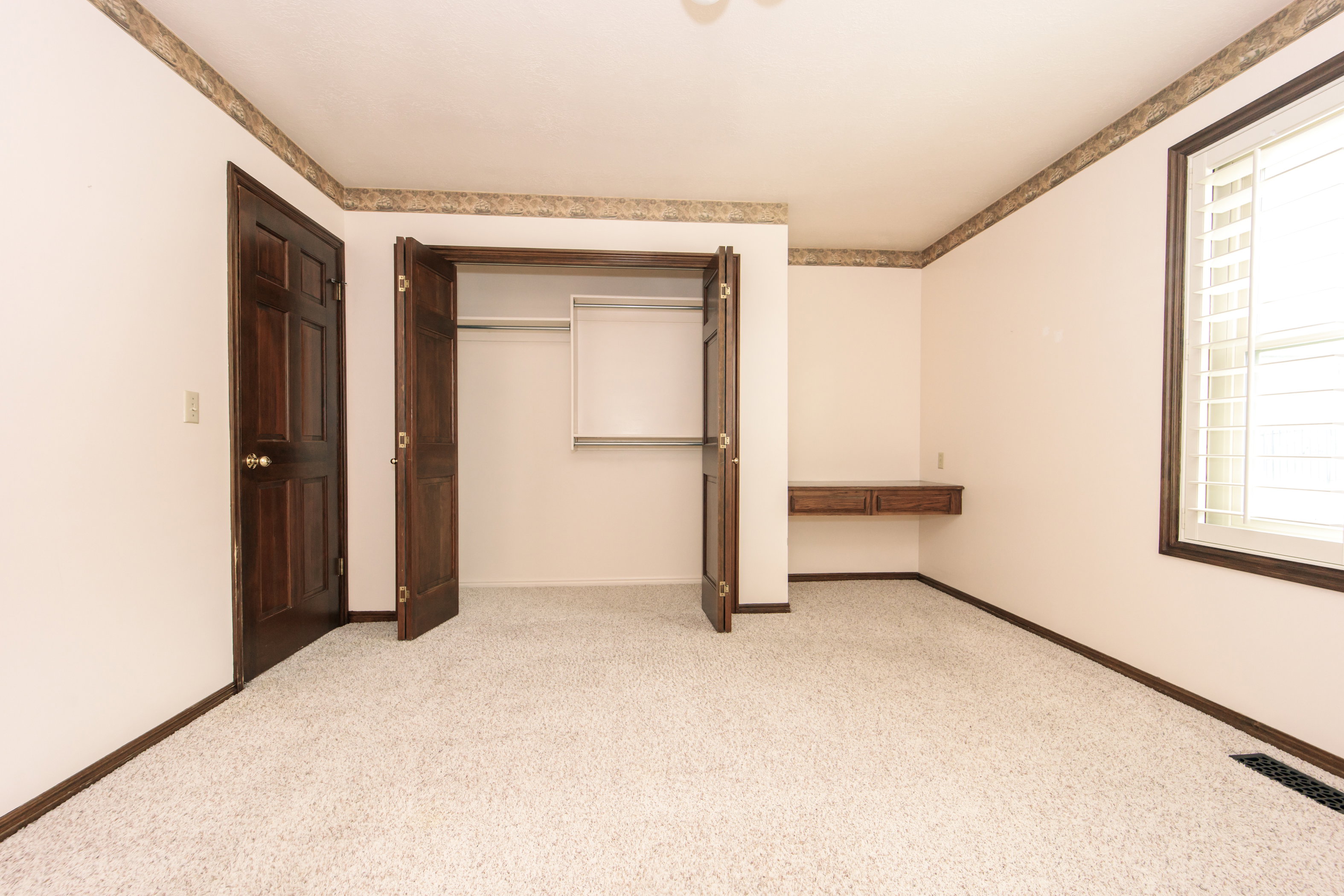 Carpeted room featuring a built-in closet with bi-fold doors, a built-in floating desk, and a window with plantation shutters