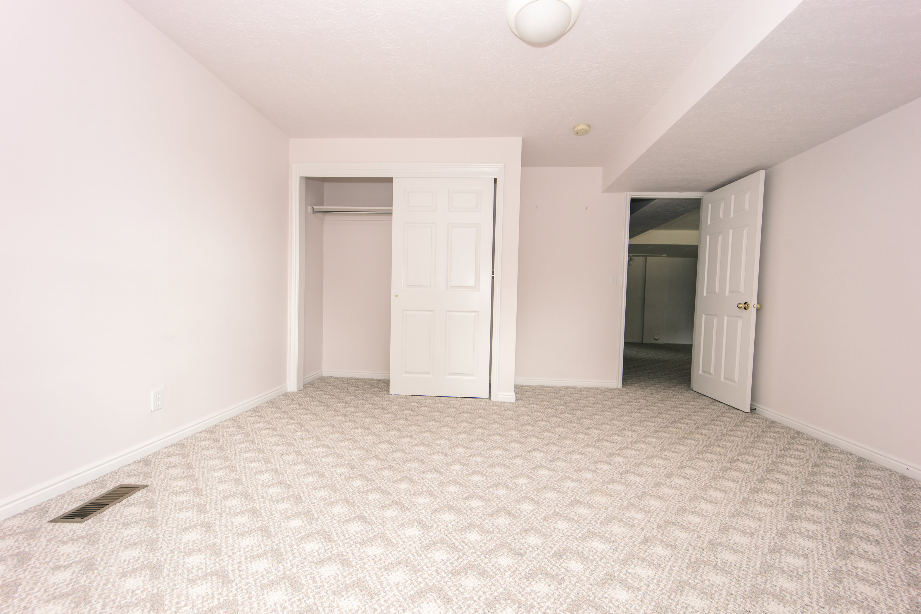 Carpeted interior space featuring a geometric pattern, white baseboards, and a built-in closet with bi-fold doors