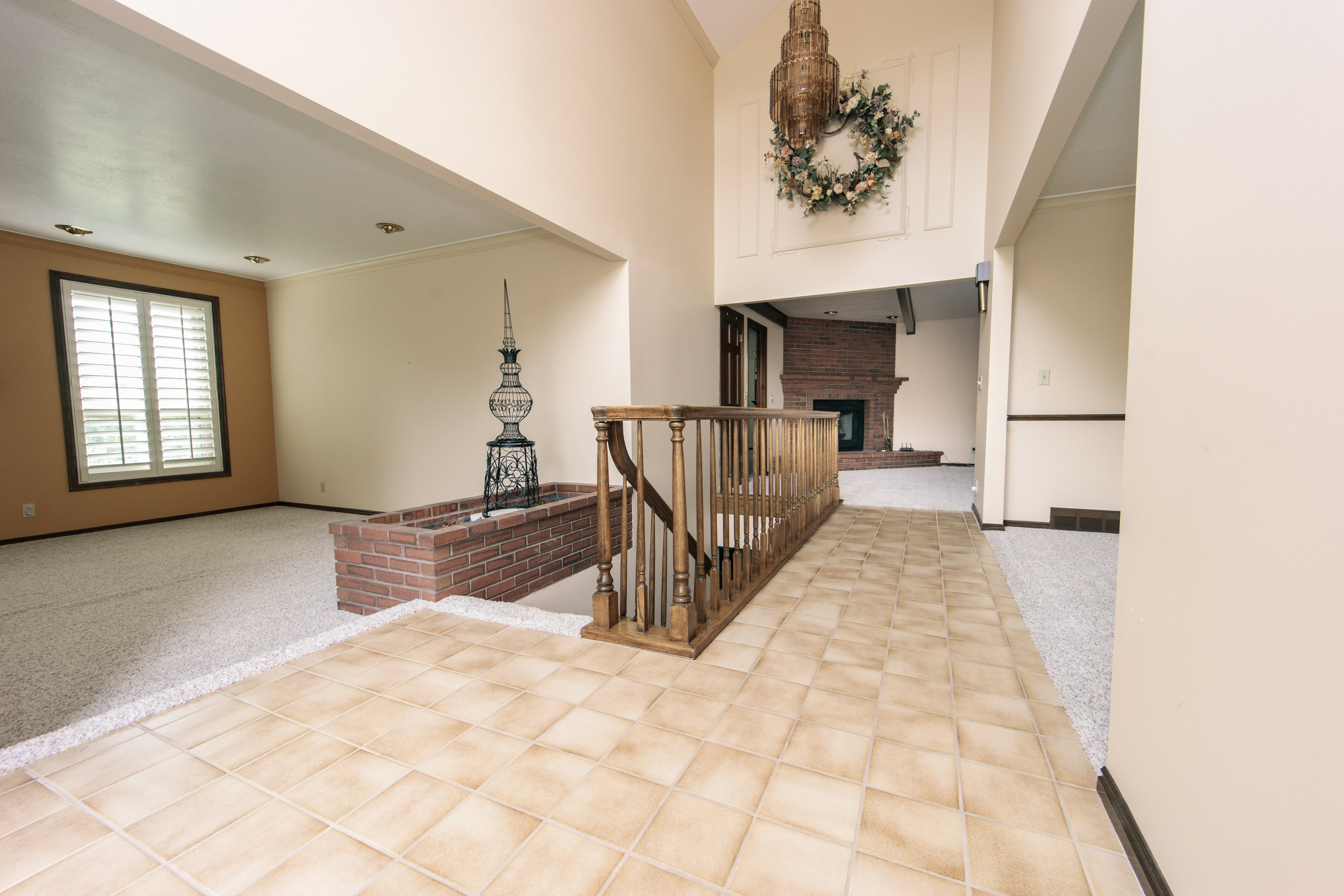 Foyer entrance featuring light-toned tile flooring, a wooden banister, and a brick-faced planter