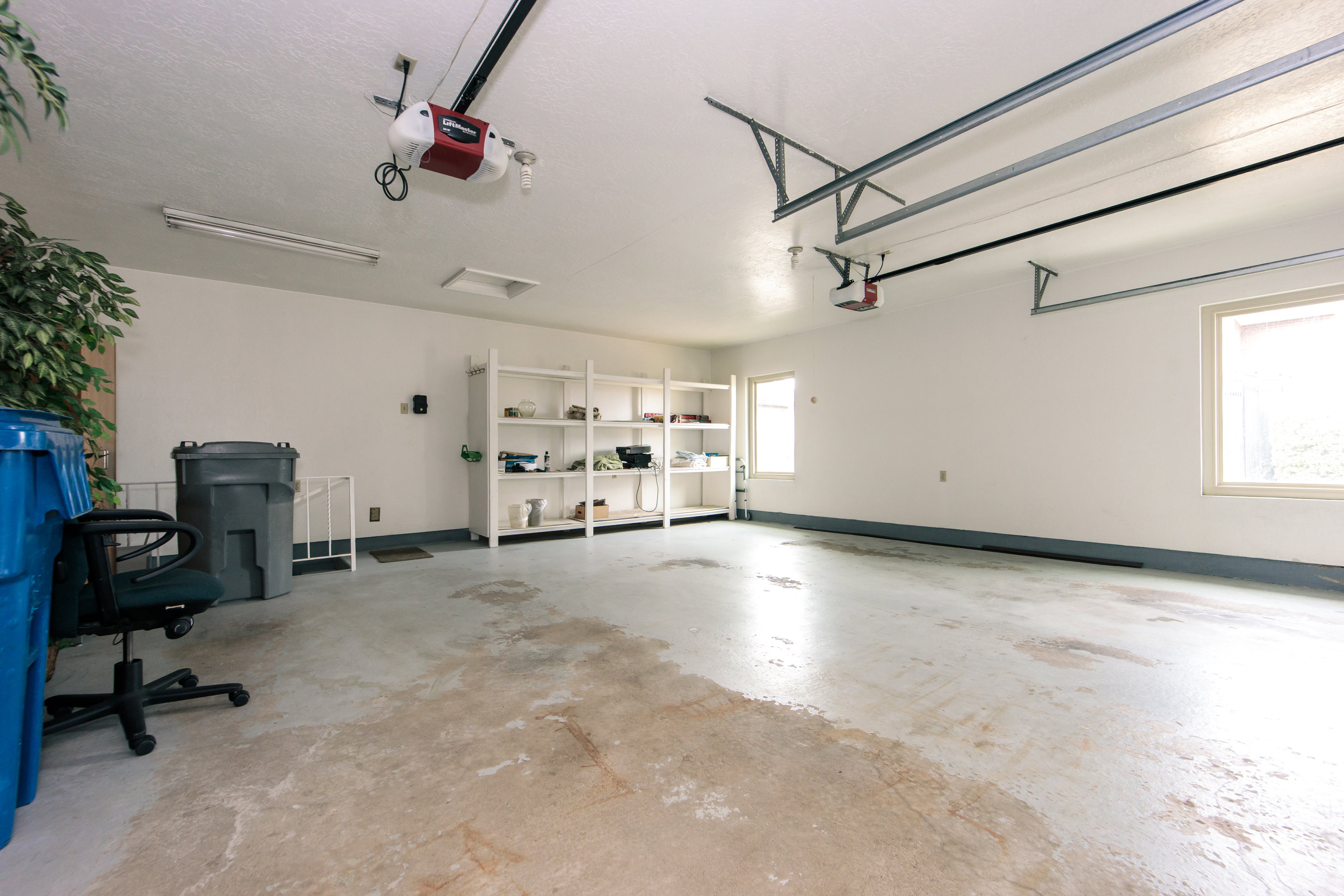 Spacious garage featuring white painted walls, two windows, two garage door openers, and built-in shelving