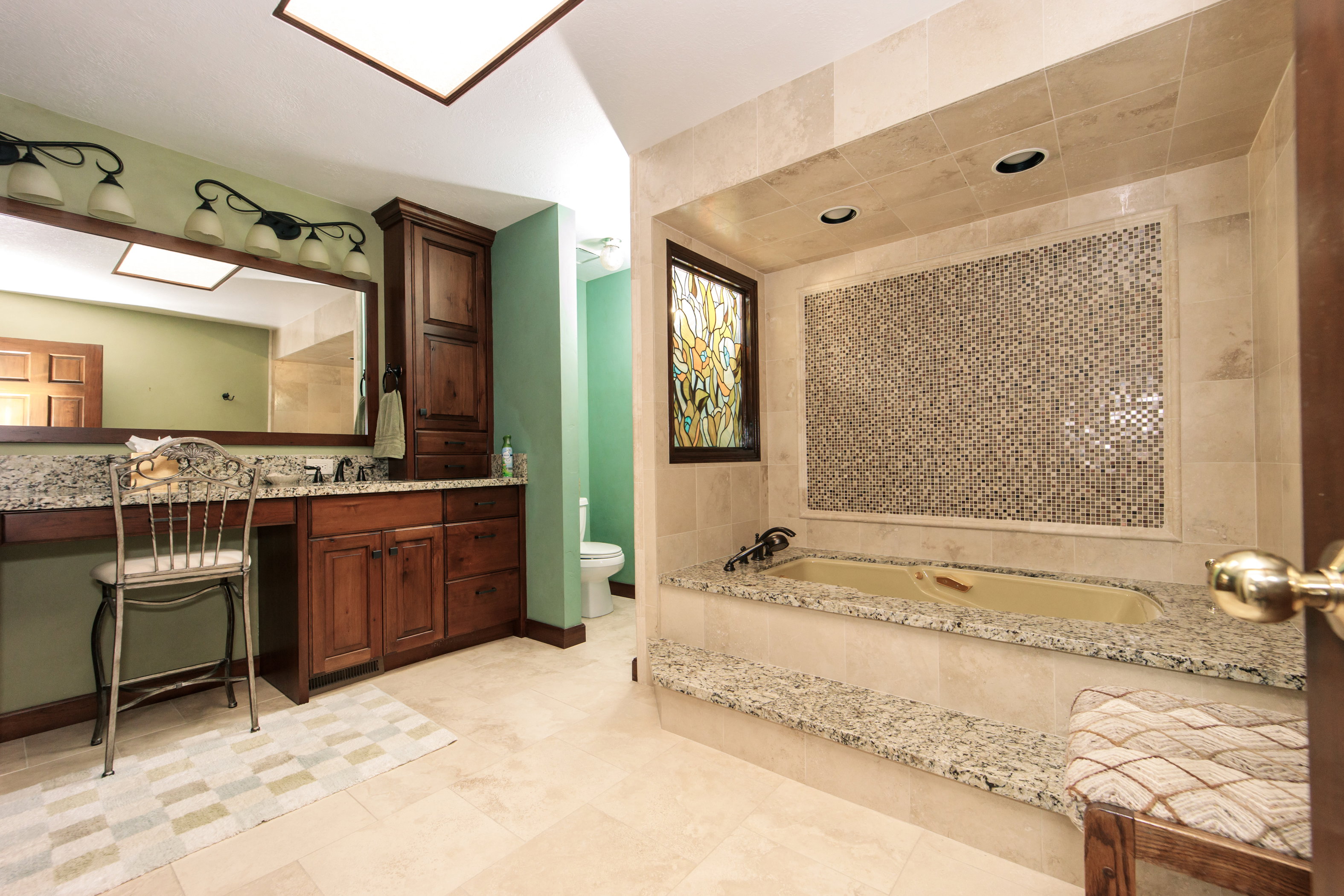 Bathroom featuring a built-in soaking tub with mosaic tile surround, wood-finish cabinetry, stone countertops, and recessed lighting