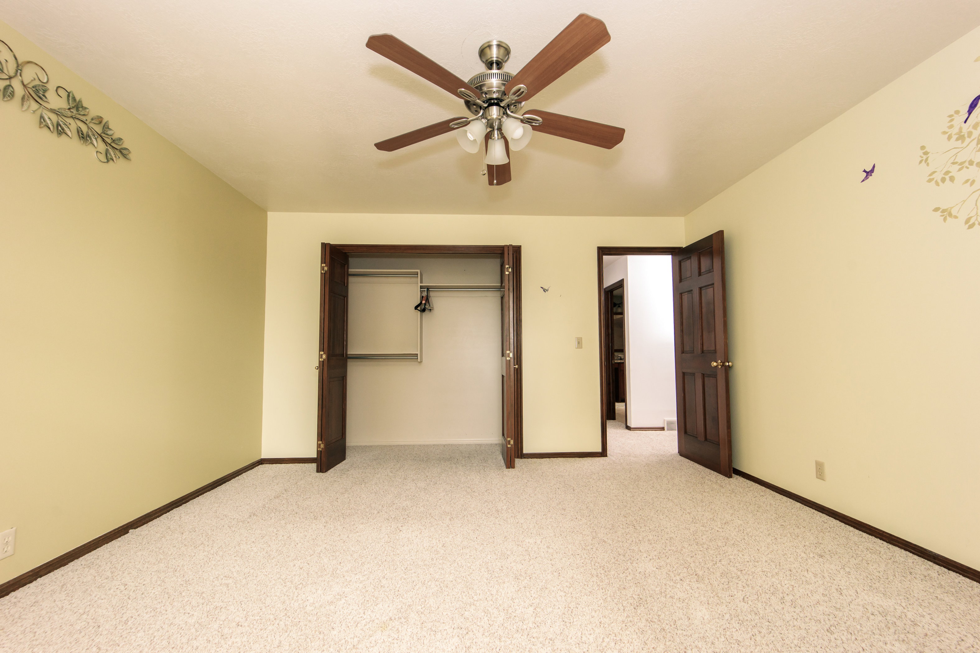Carpeted room featuring a ceiling fan with integrated lighting, a spacious closet with bi-fold doors, and a solid wood paneled door