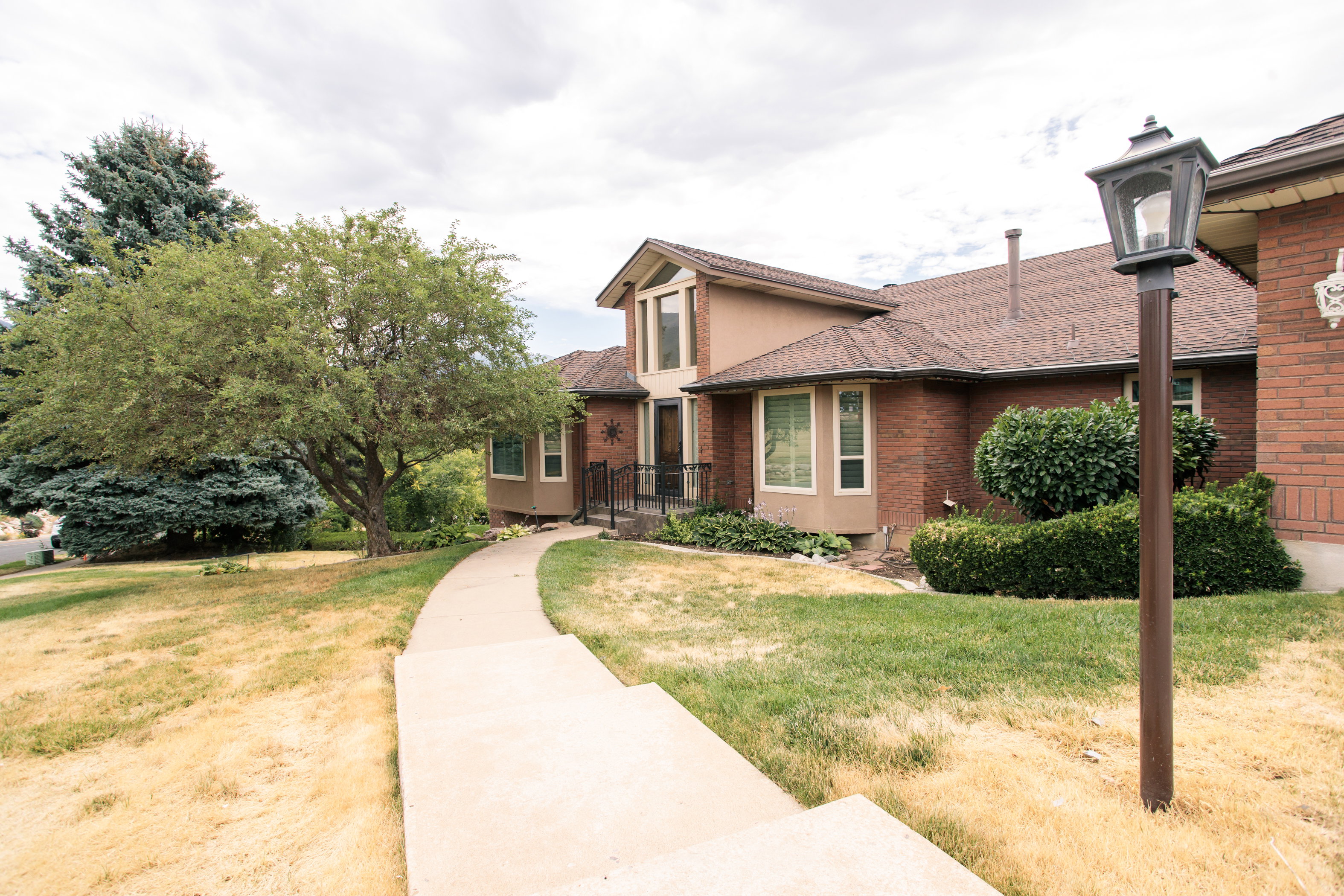 Traditional brick residence featuring a brown shingle roof, bay windows, and a concrete pathway leading to the entrance