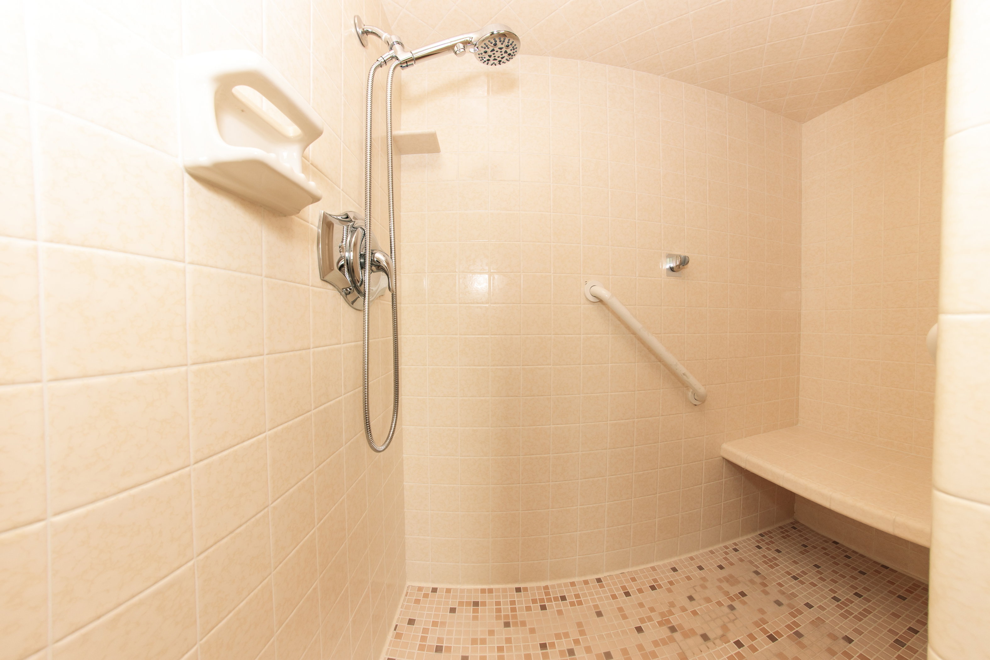 Curved shower enclosure with full-height beige wall tiling and a built-in shower bench