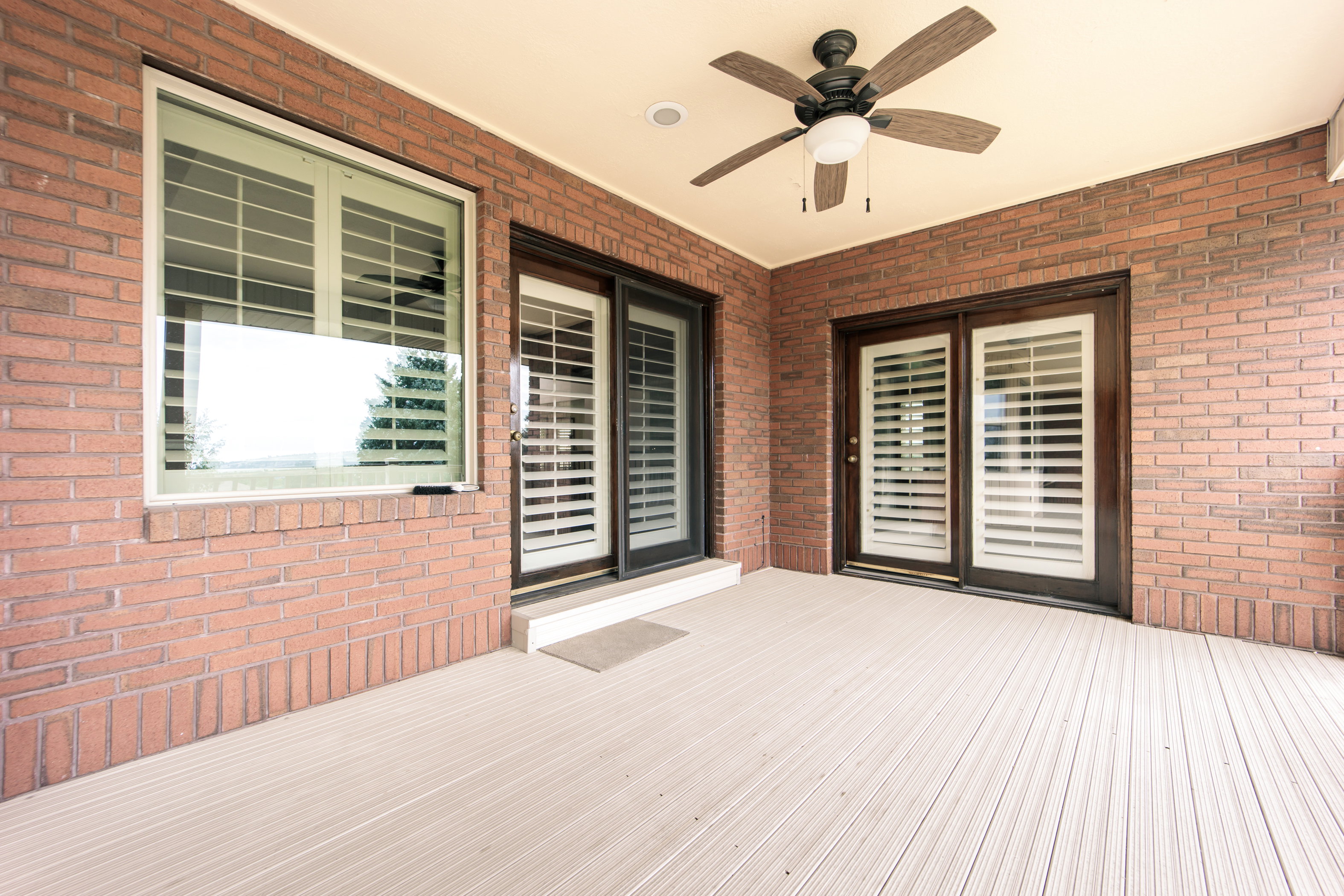 Covered outdoor living space featuring brick exterior walls and a light-colored composite deck