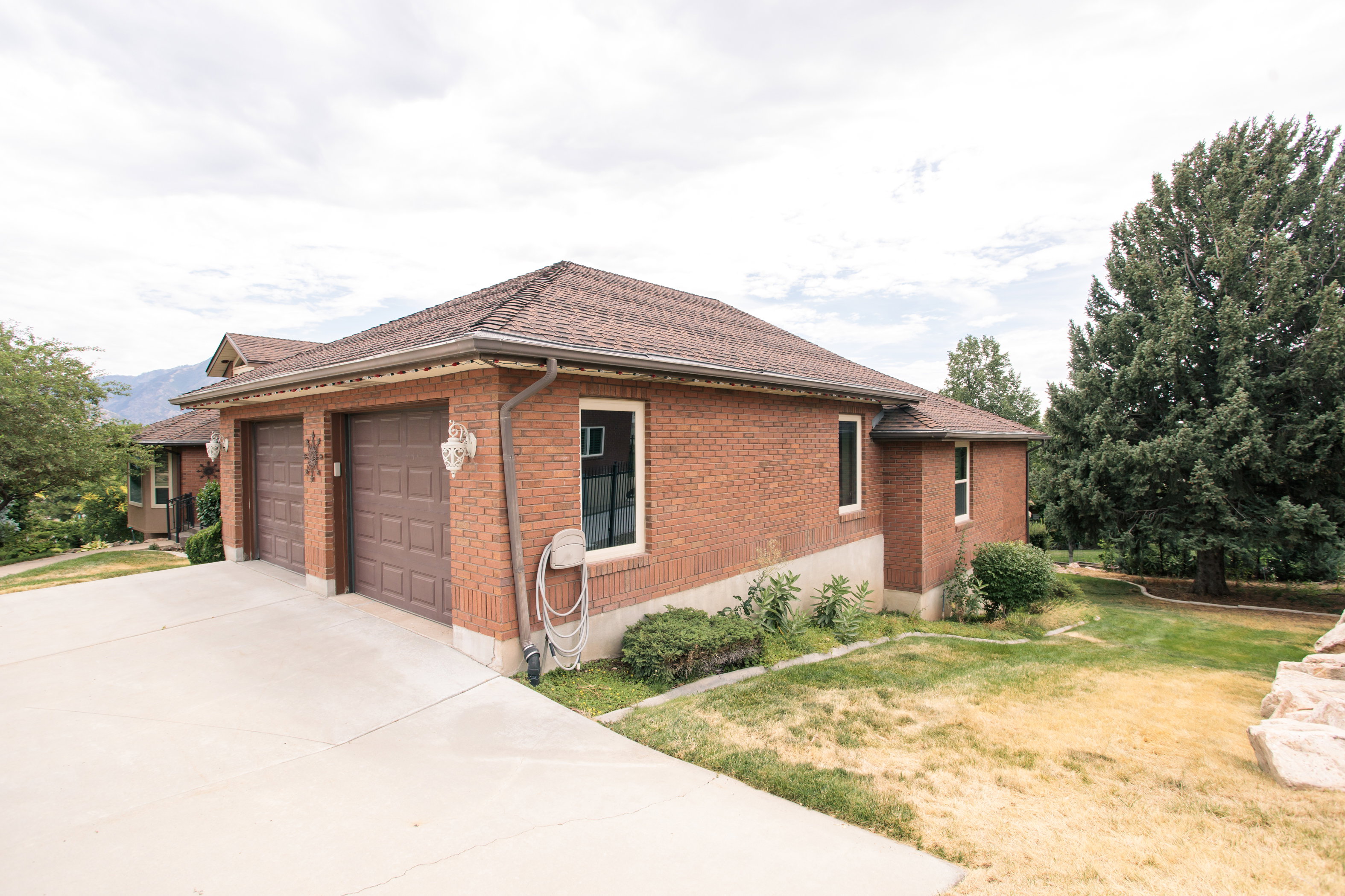 Brick exterior featuring a two-car garage with panel doors, concrete driveway, and a shingled roof