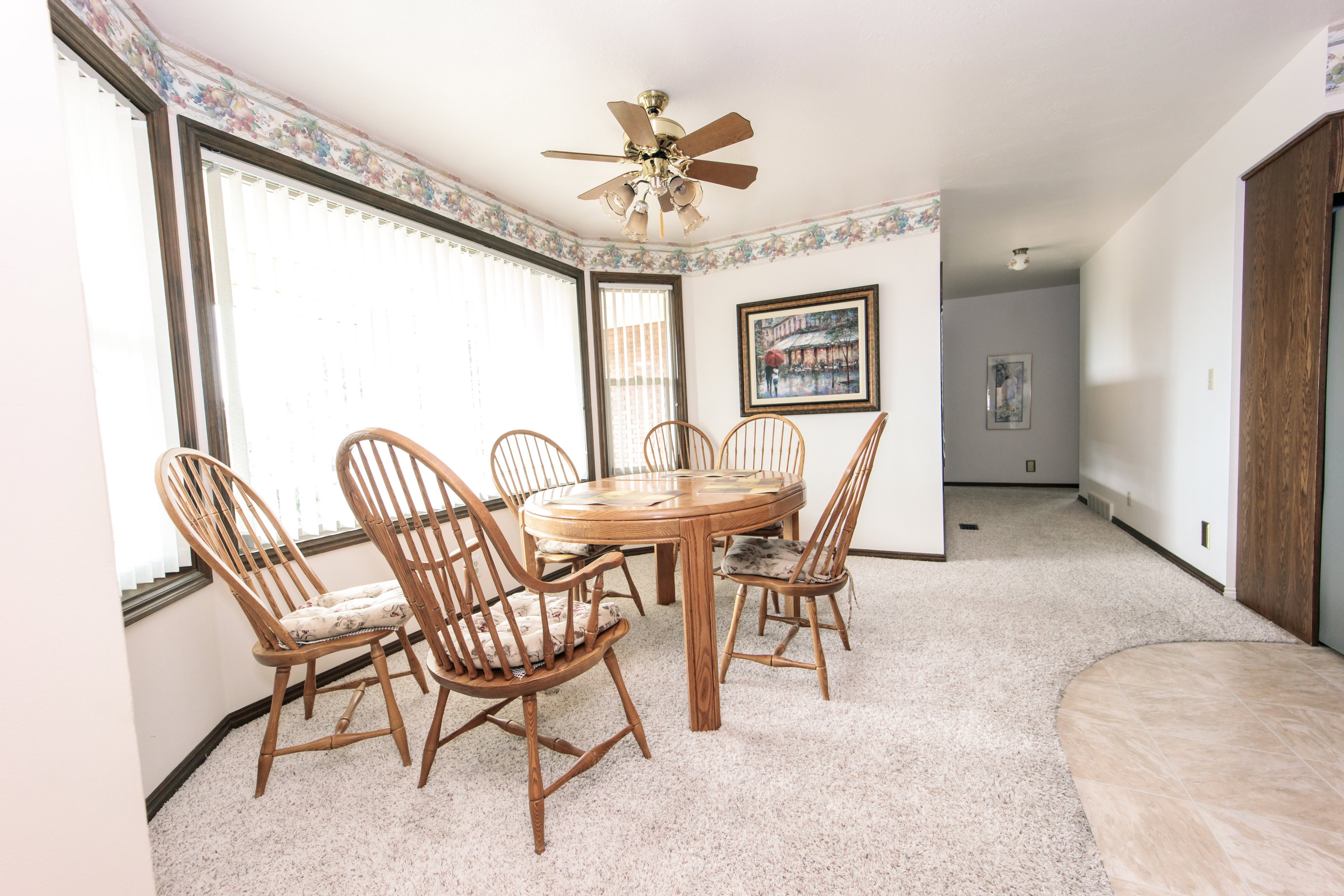Bay window with vertical blinds, textured wall-to-wall carpeting, ceiling fan with integrated lighting, and a wood-finish built-in cabinet