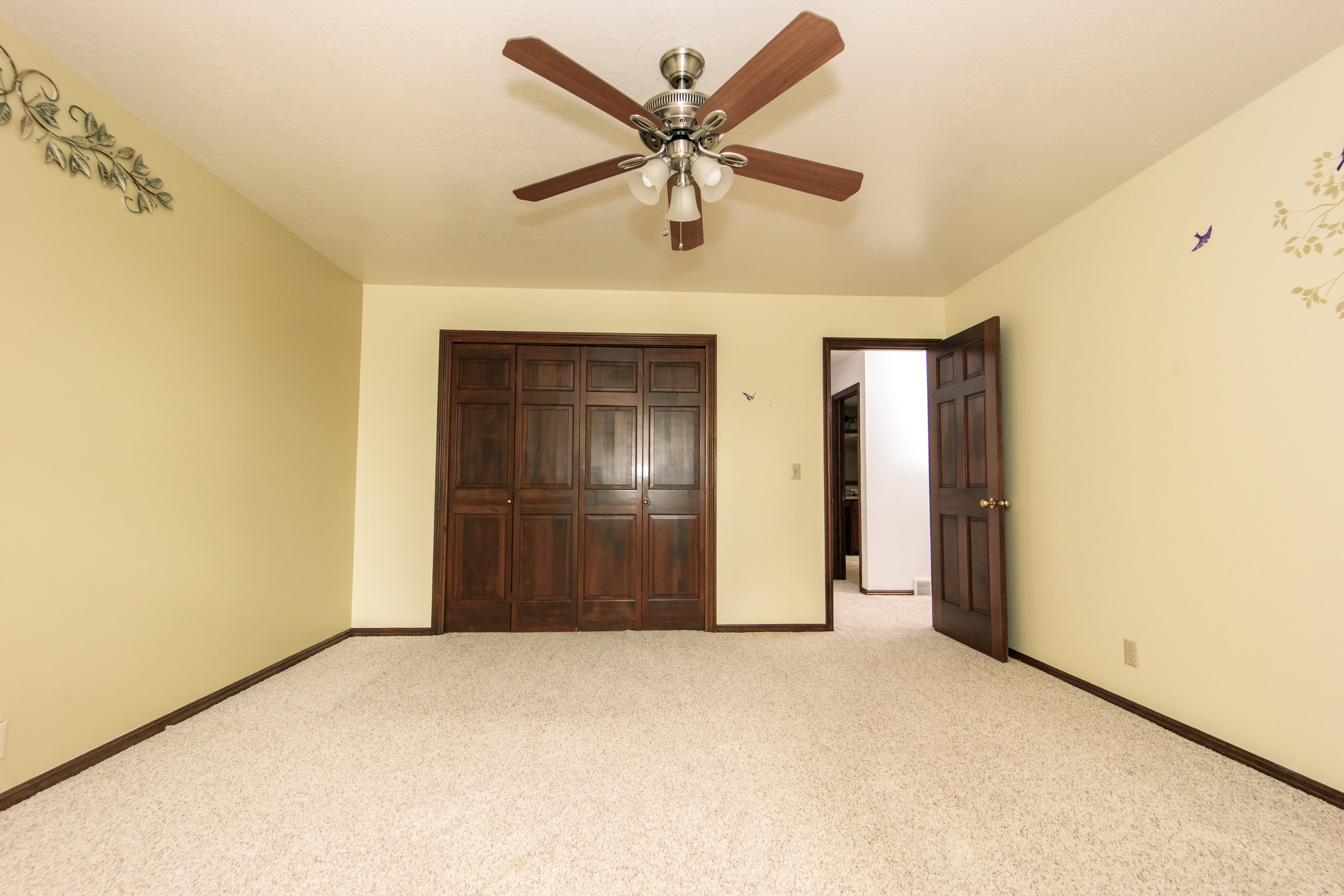 Carpeted room featuring a ceiling fan with integrated lighting, dark wood bi-fold closet doors, and dark wood trim