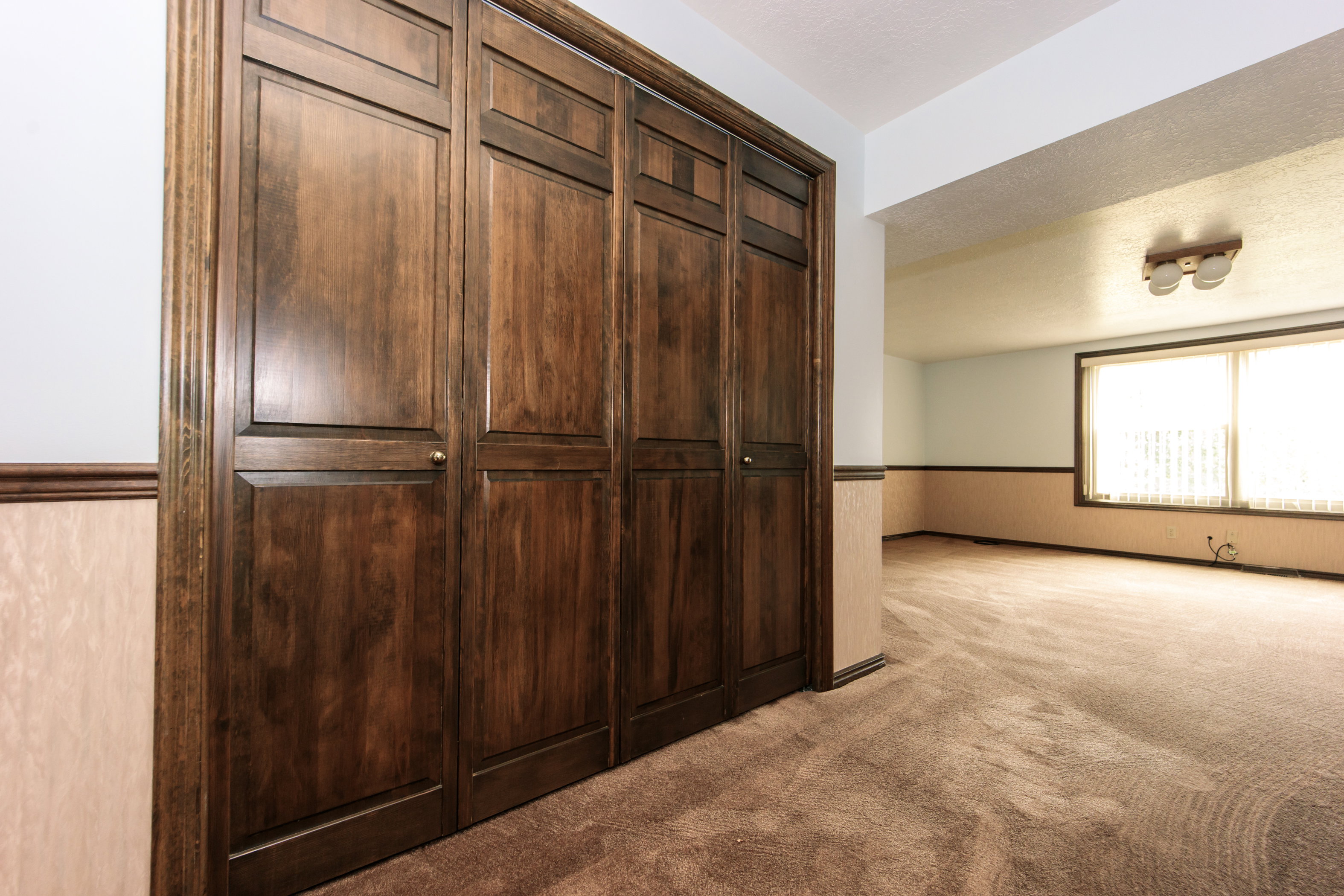 Wood-panel bi-fold closet doors with brass hardware, textured wall paneling, and wall-to-wall carpeting throughout