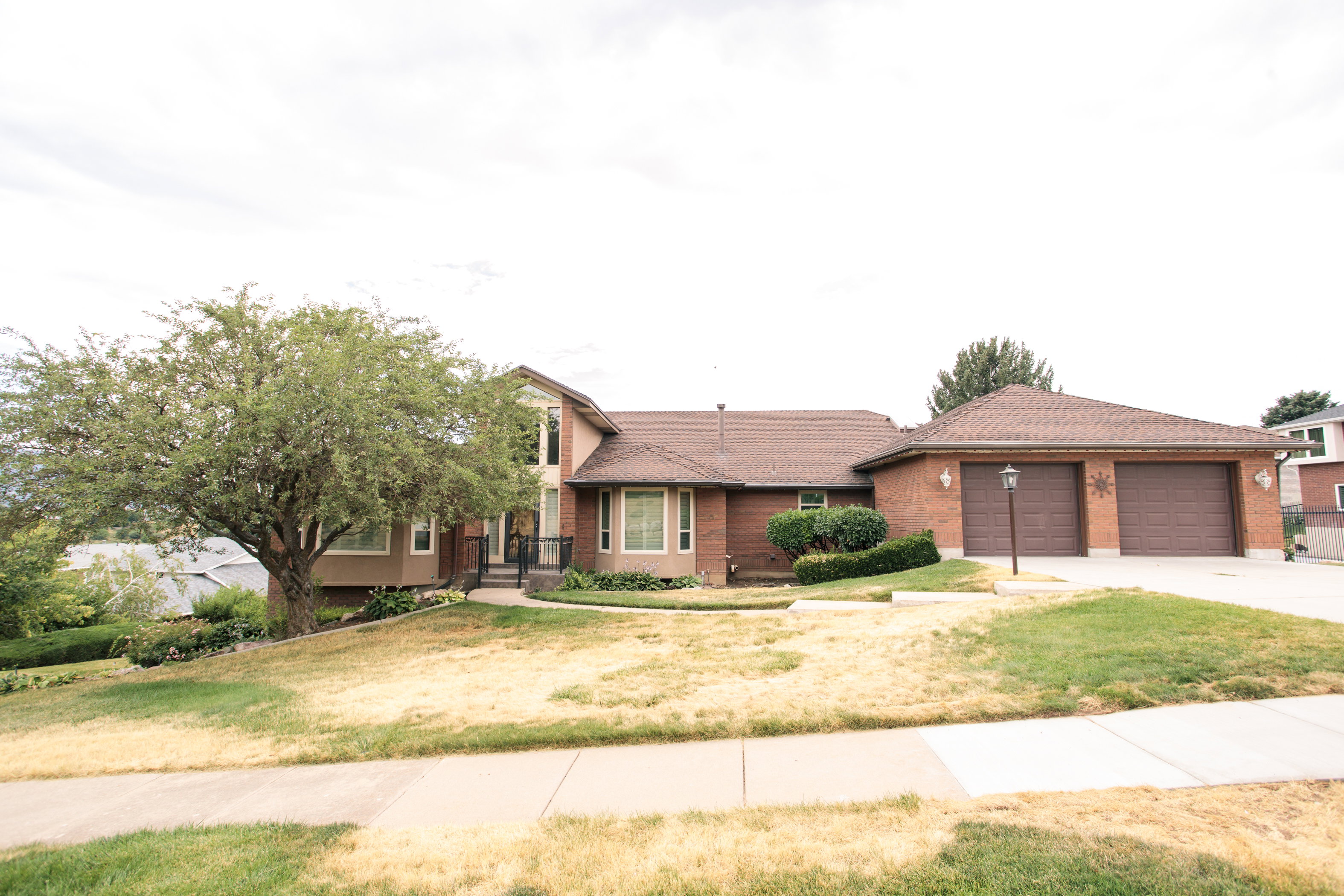 Brick exterior home featuring a two-car garage, mature front yard tree, and an inviting front entrance