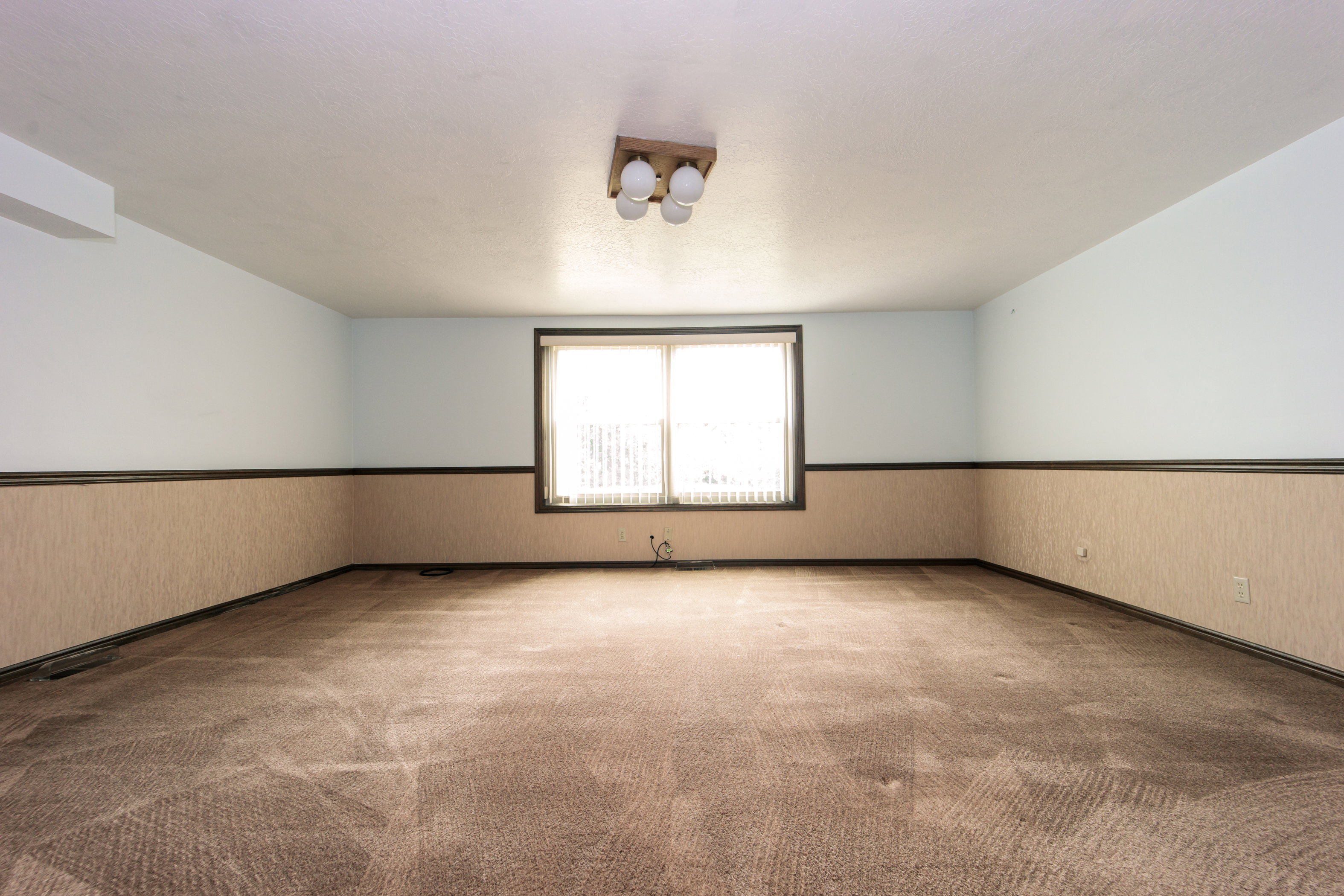 Spacious room featuring broadloom carpeting, a window with vertical blinds, and a ceiling-mounted light fixture