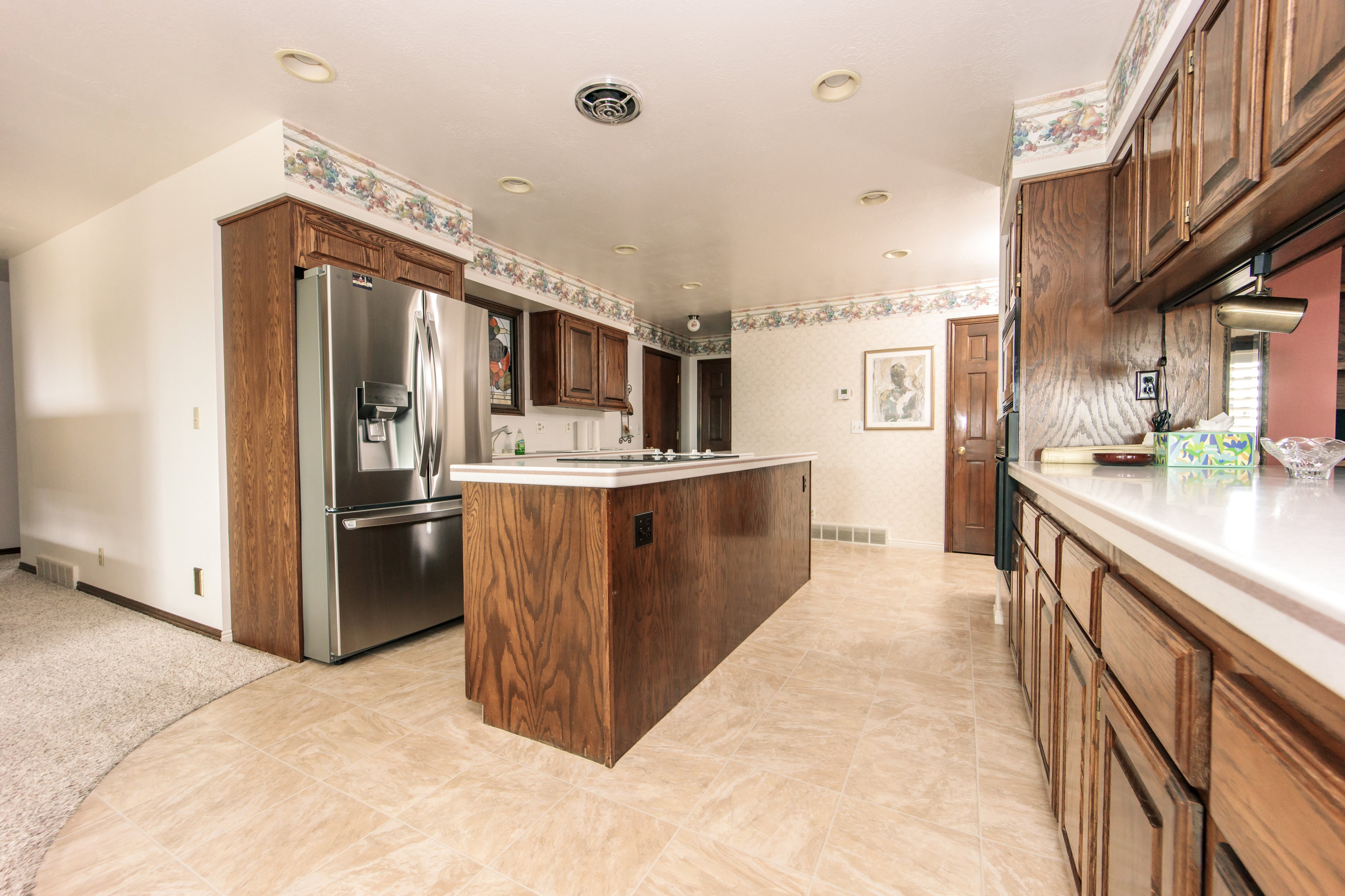 Kitchen featuring light-toned tile flooring, wood cabinetry, an integrated stainless steel refrigerator, white countertops, and recessed lighting