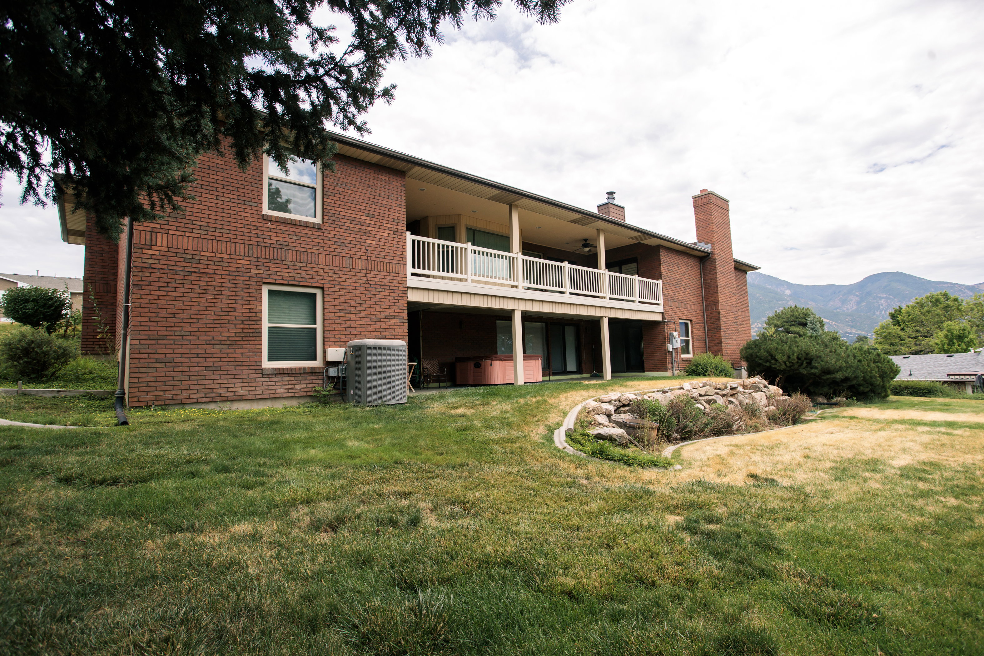Brick exterior residence featuring a covered balcony with white railing, lower level patio access, and a rock-lined garden bed