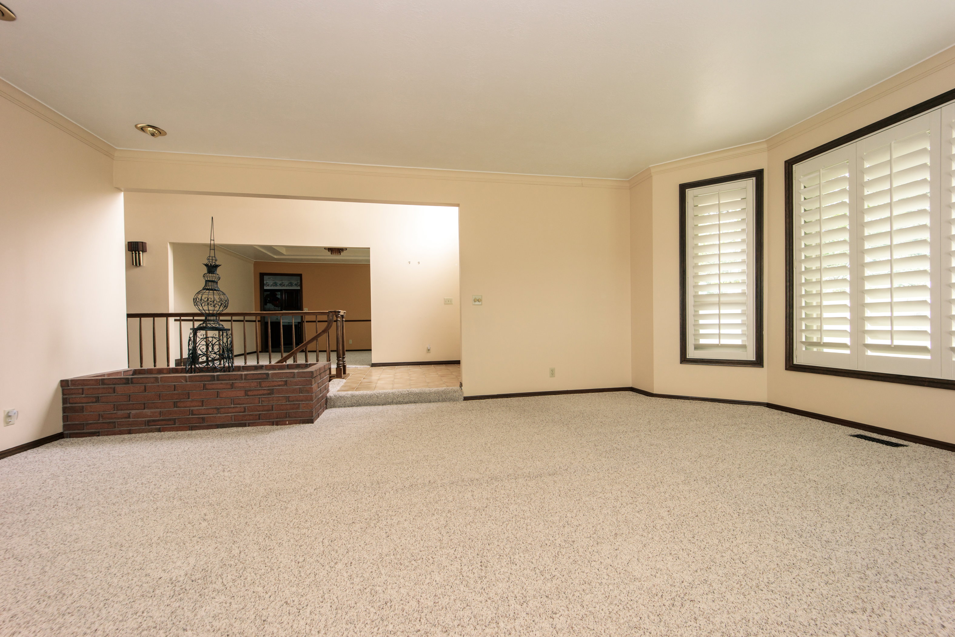 Spacious living area featuring neutral carpeting, a decorative brick planter, and a half-wall with iron railing