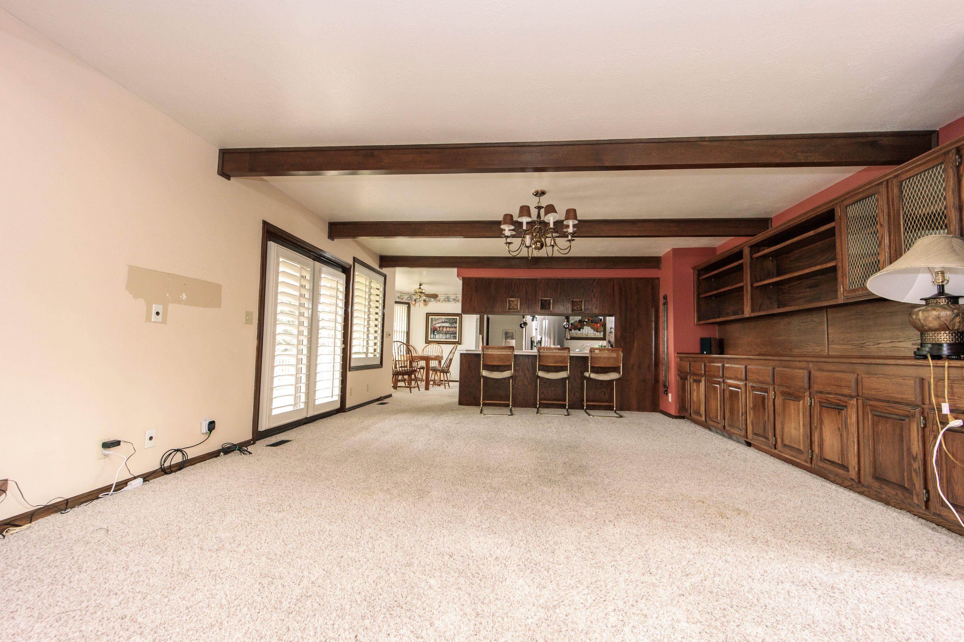 Spacious room featuring exposed wood beams, wall-to-wall carpeting, and a built-in wood cabinetry unit with glass-fronted upper cabinets