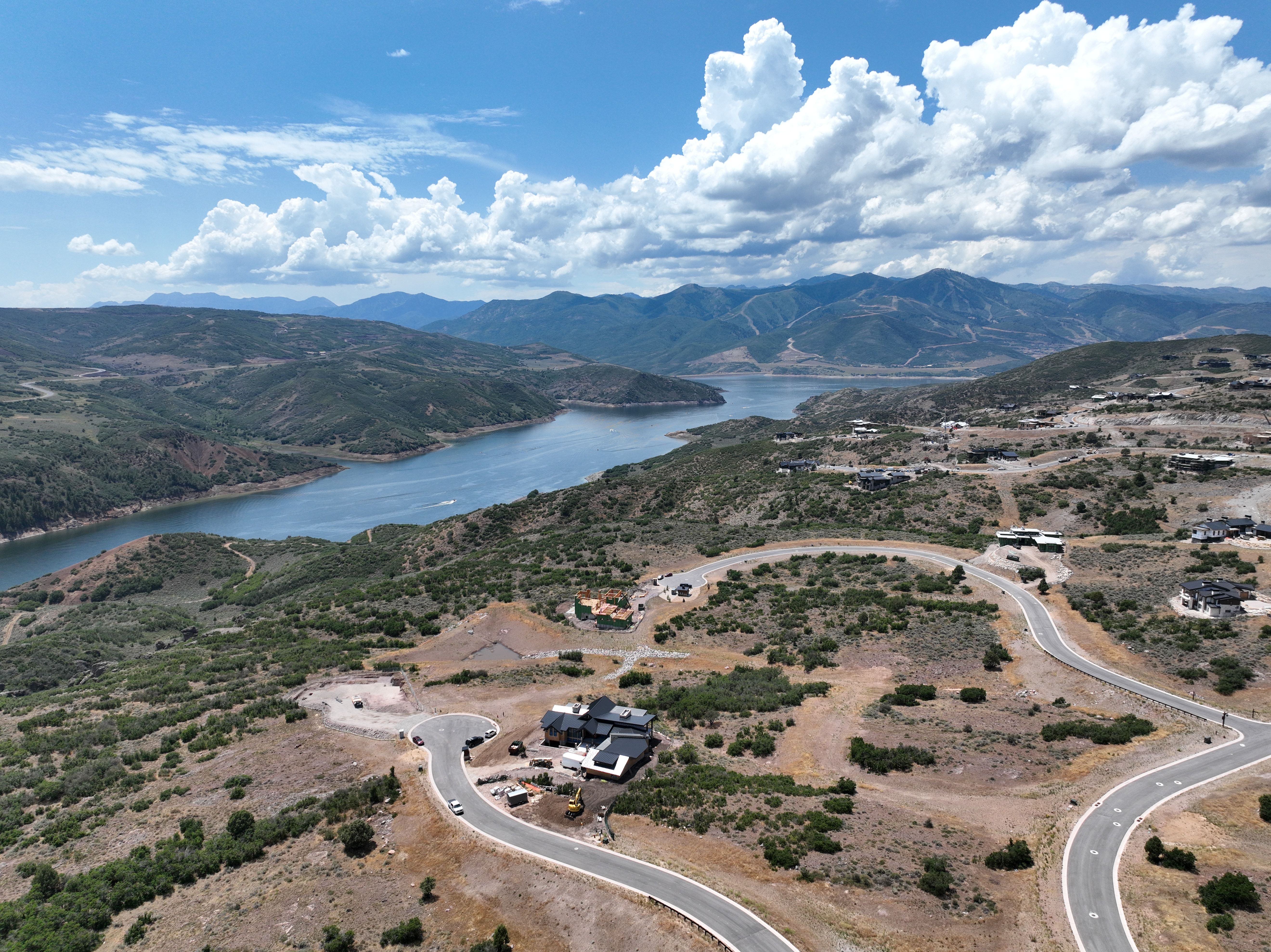 Expansive elevated property featuring a paved road, scattered vegetation, a substantial body of water, and distant mountains