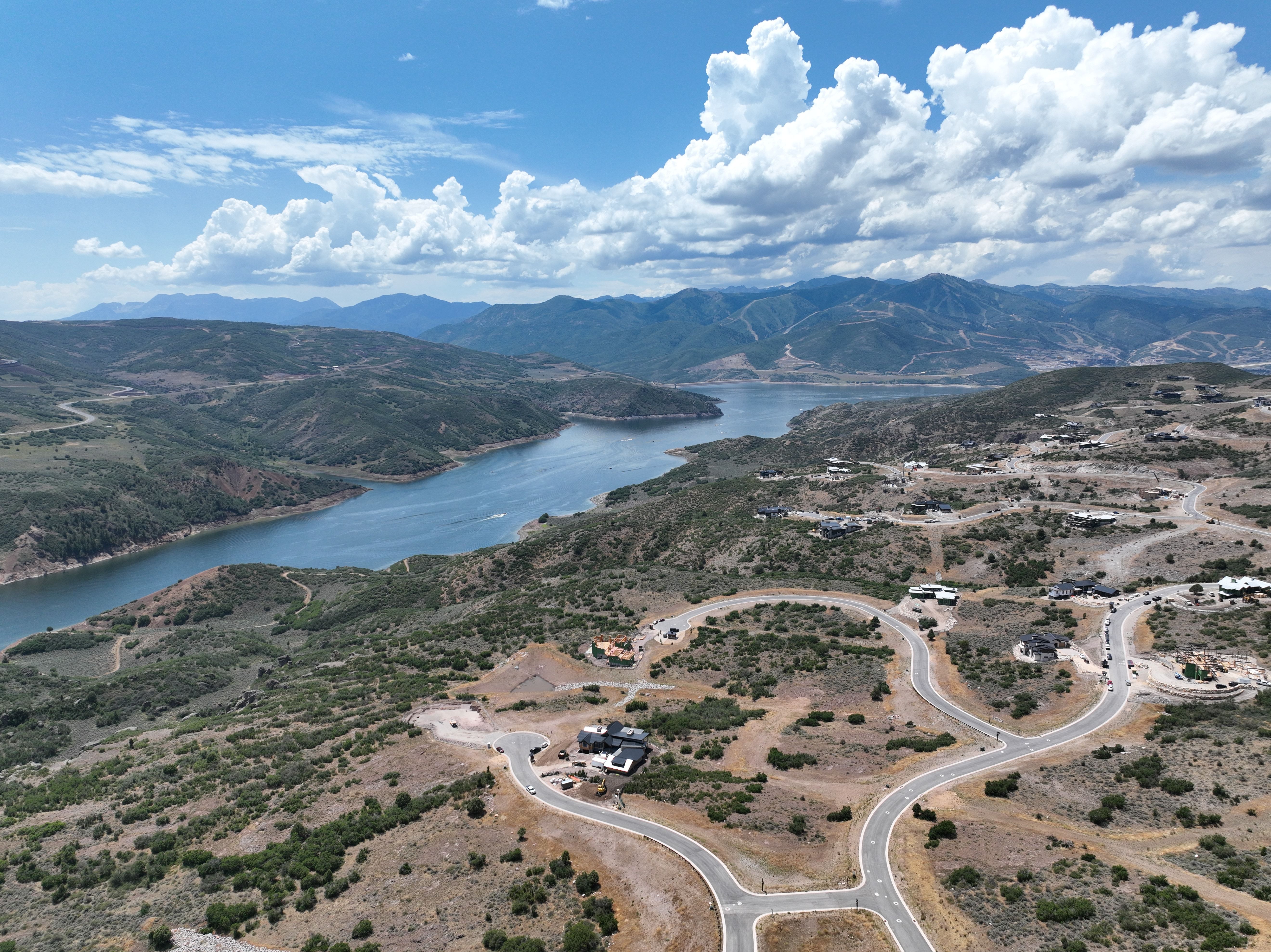 Aerial landscape featuring a large body of water, distant mountains, and winding paved roads