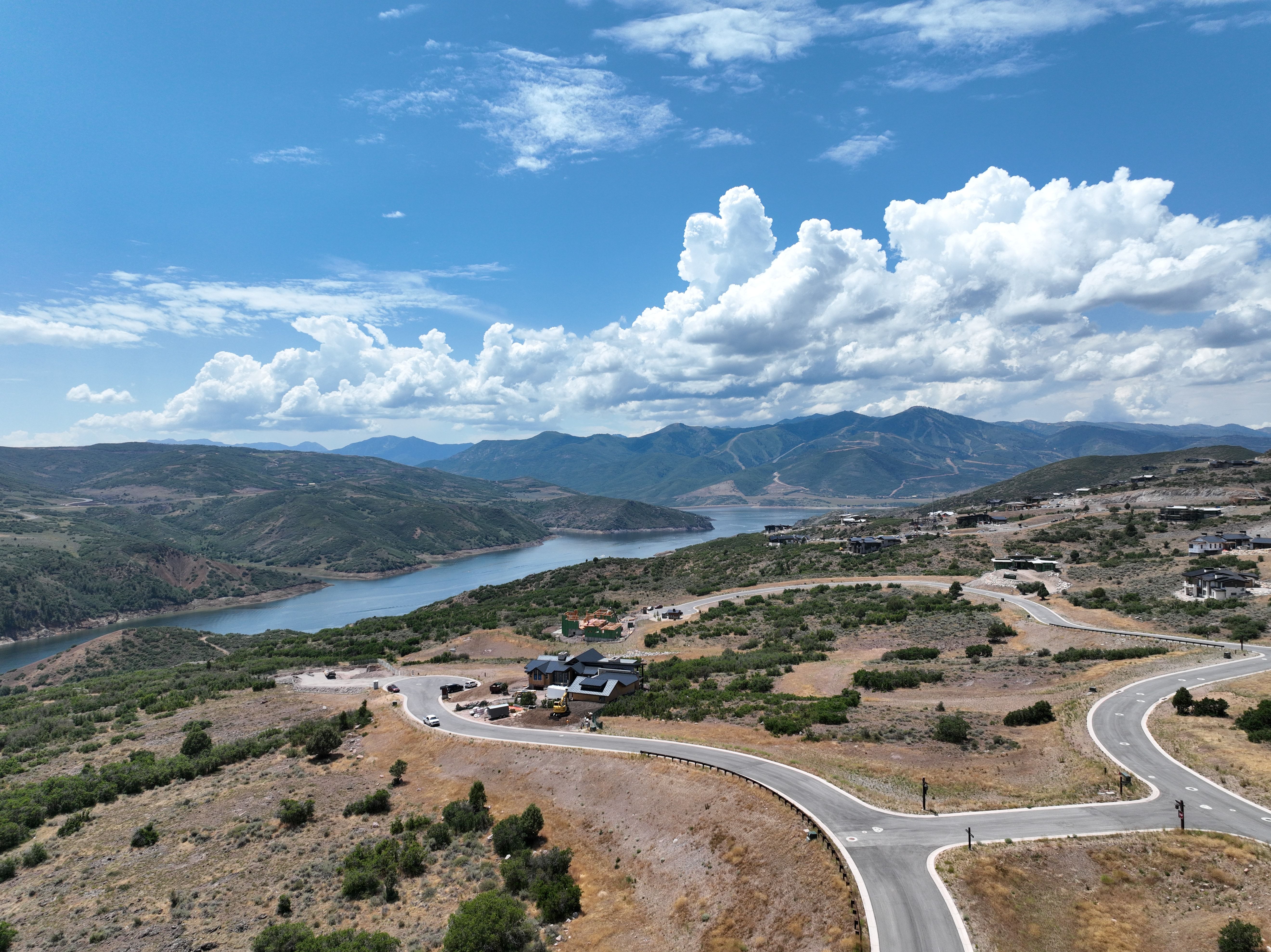 Sweeping aerial perspective showcasing a mountainous reservoir backdrop, undeveloped land, winding paved roads, and several residential structures