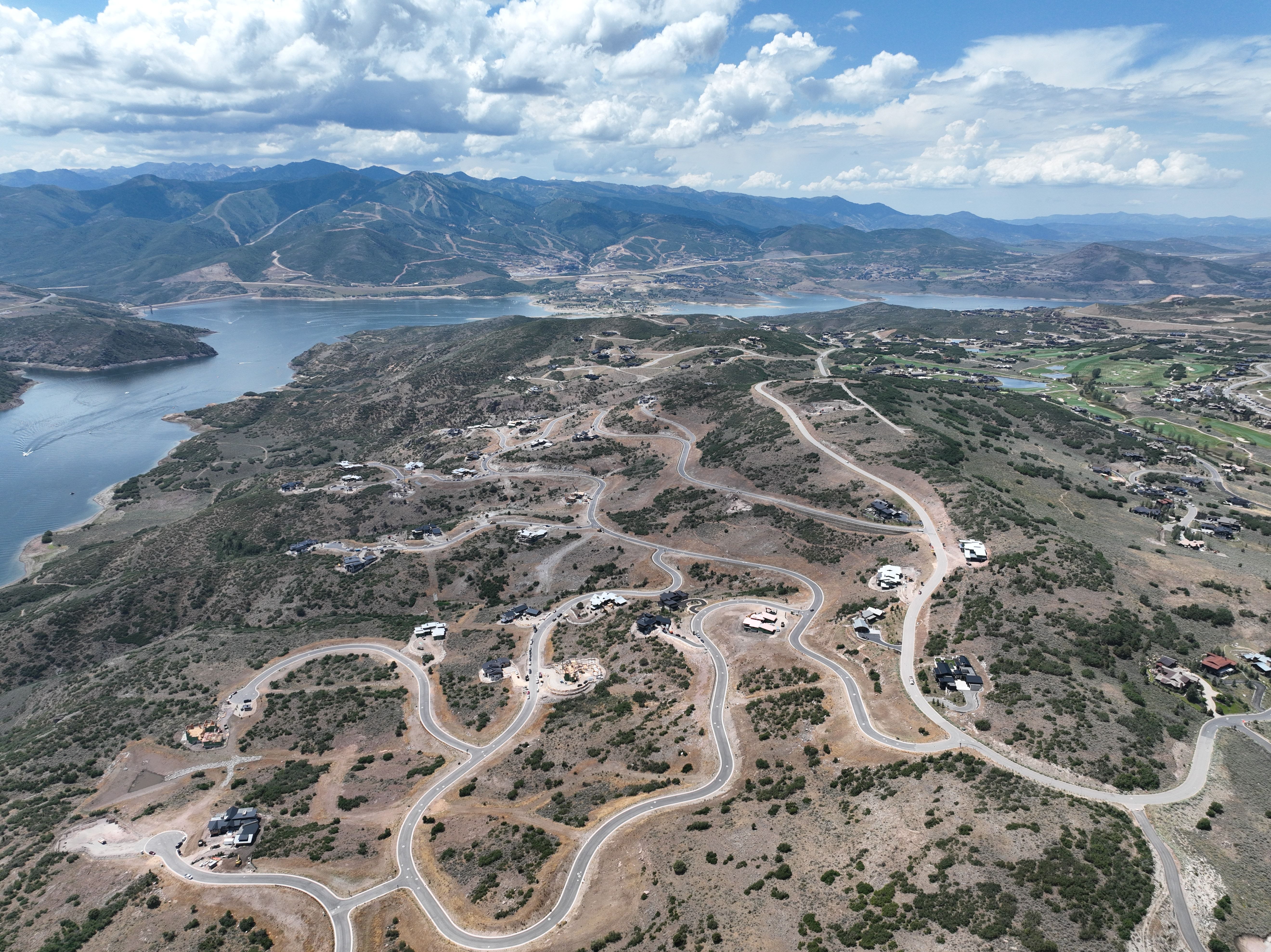 Expansive aerial showcasing a large lake, mountainous terrain, and winding roads