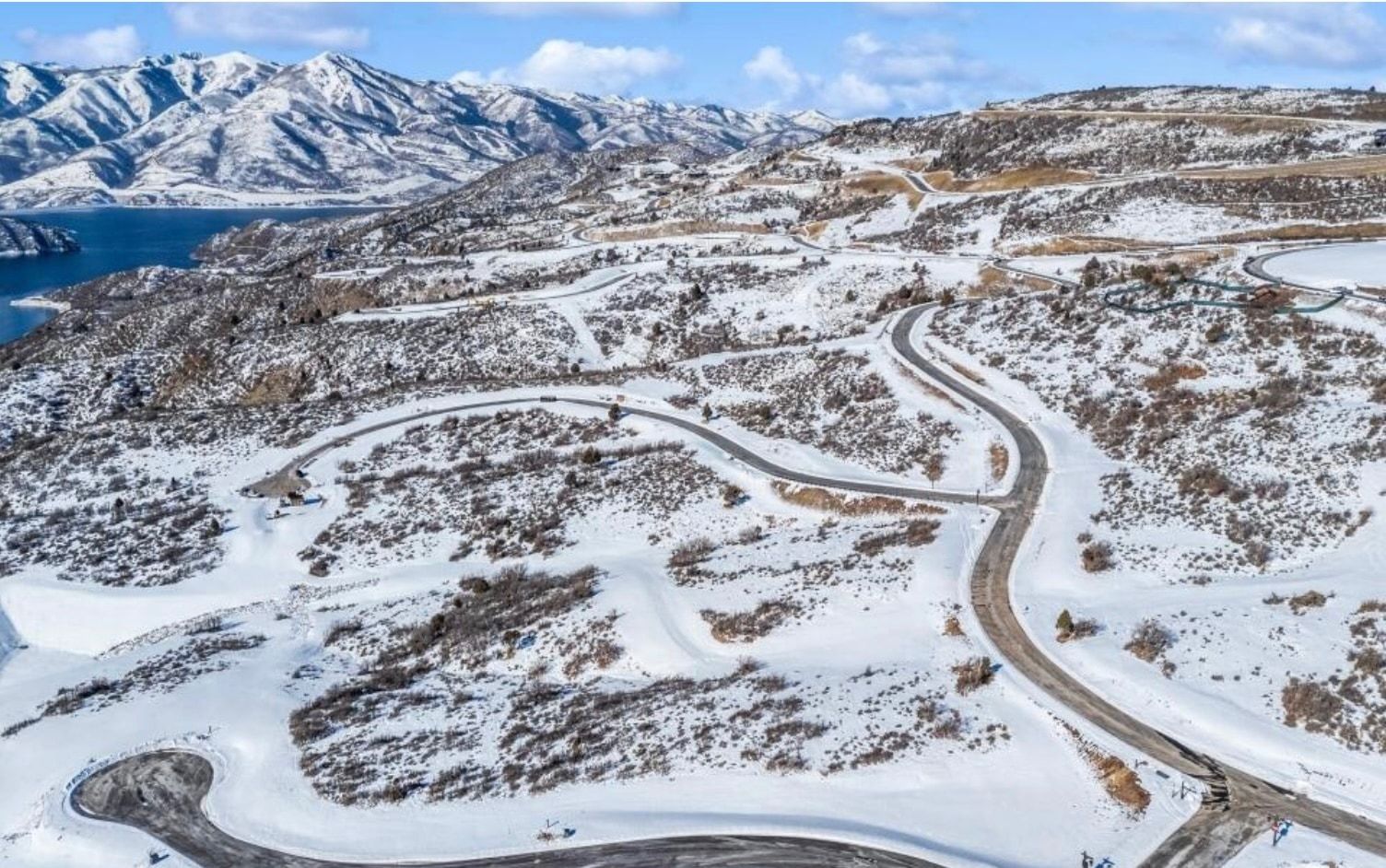 Expansive snow-covered landscape with a prominent body of water, snow-capped mountains, and a network of paved roads