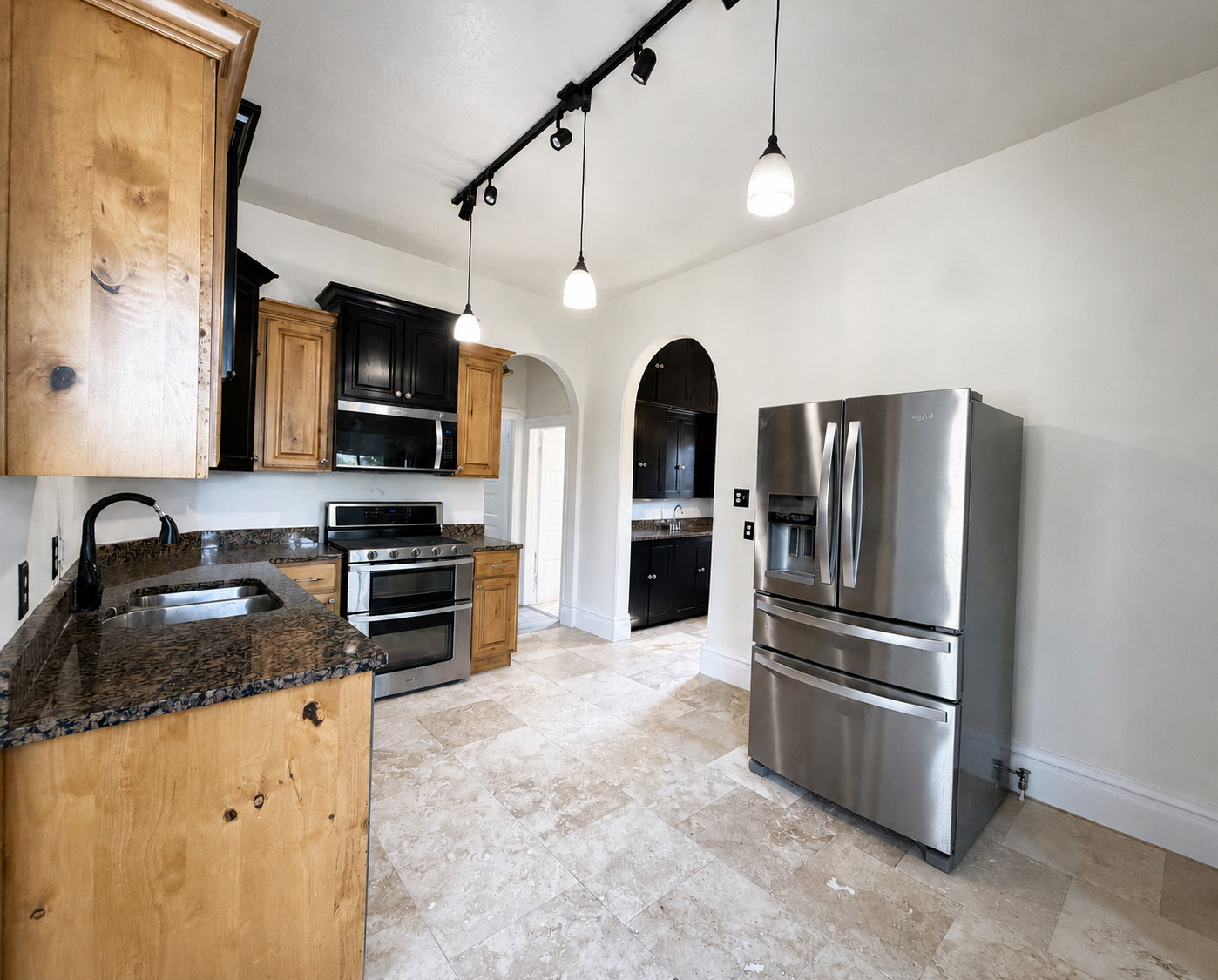 Kitchen featuring stainless steel appliances, dual-tone cabinetry, granite countertops, and stone tile flooring