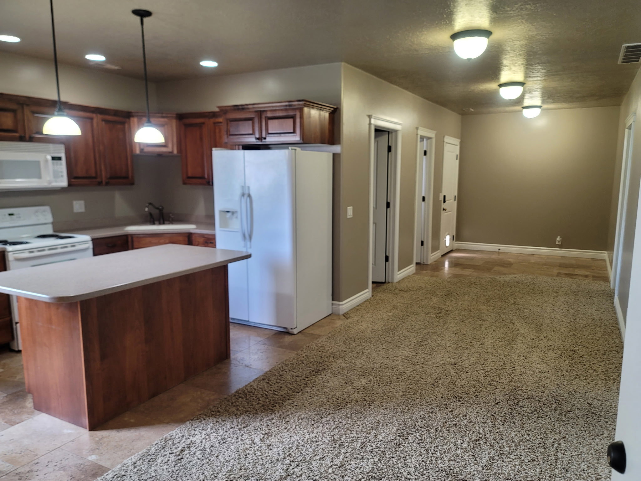 Functional kitchen featuring wood cabinetry, white appliances, and a central island with a light-toned countertop