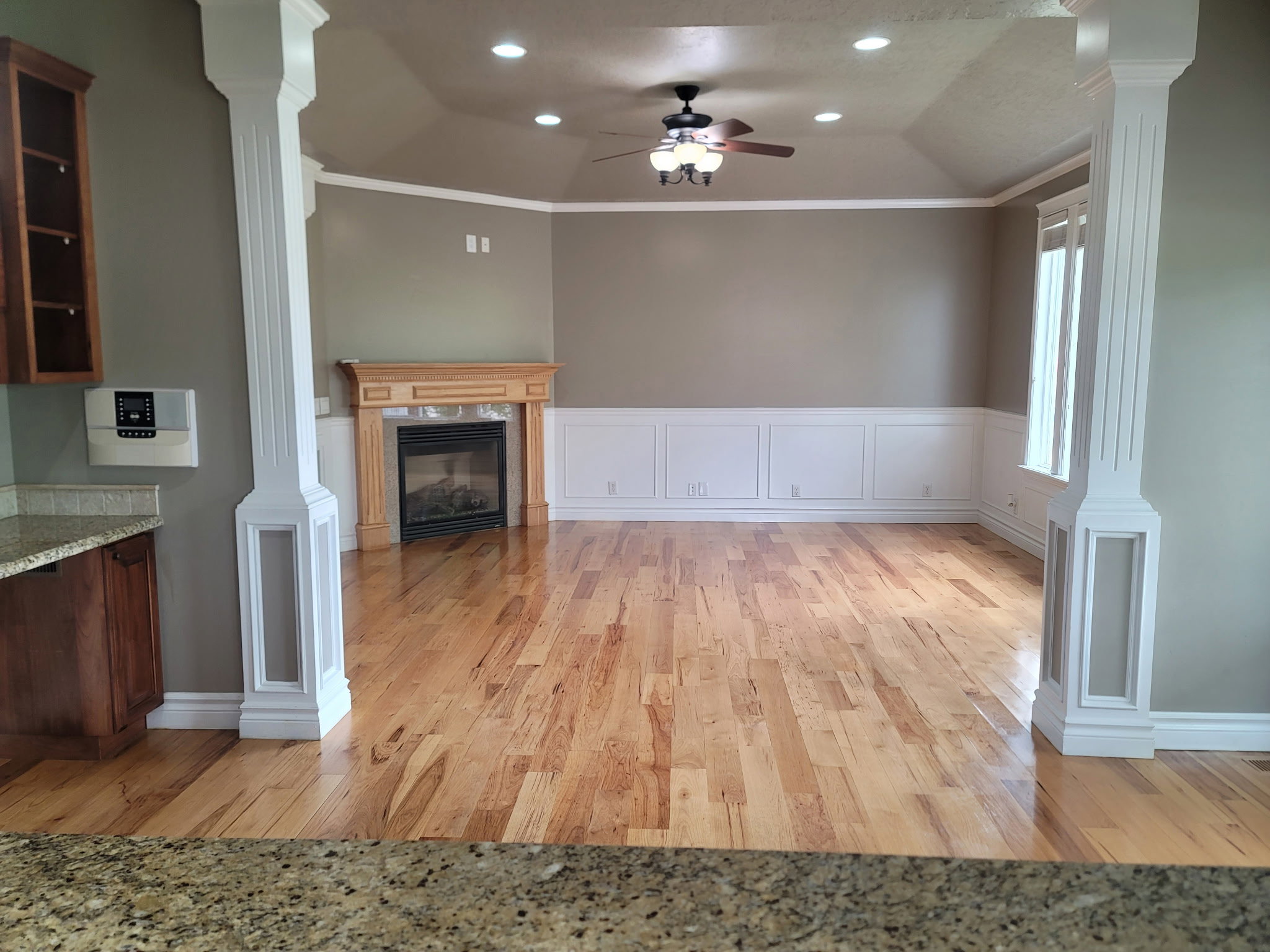 Spacious living area featuring polished wood flooring, a decorative fireplace with a natural wood mantel, recessed lighting, and a ceiling fan