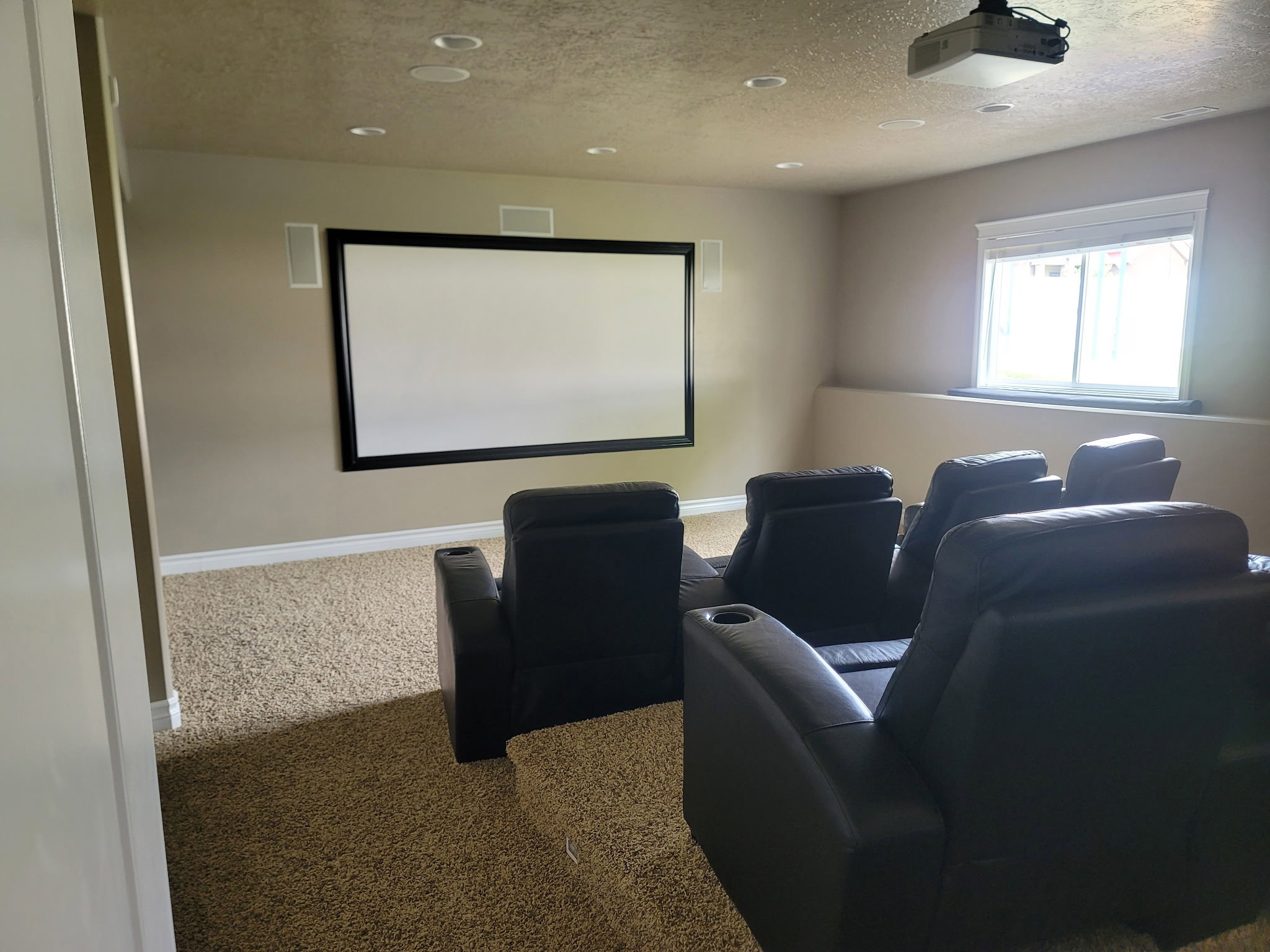 Dedicated entertainment space featuring a large projection screen, built-in ceiling speakers, recessed lighting, and a window with white blinds