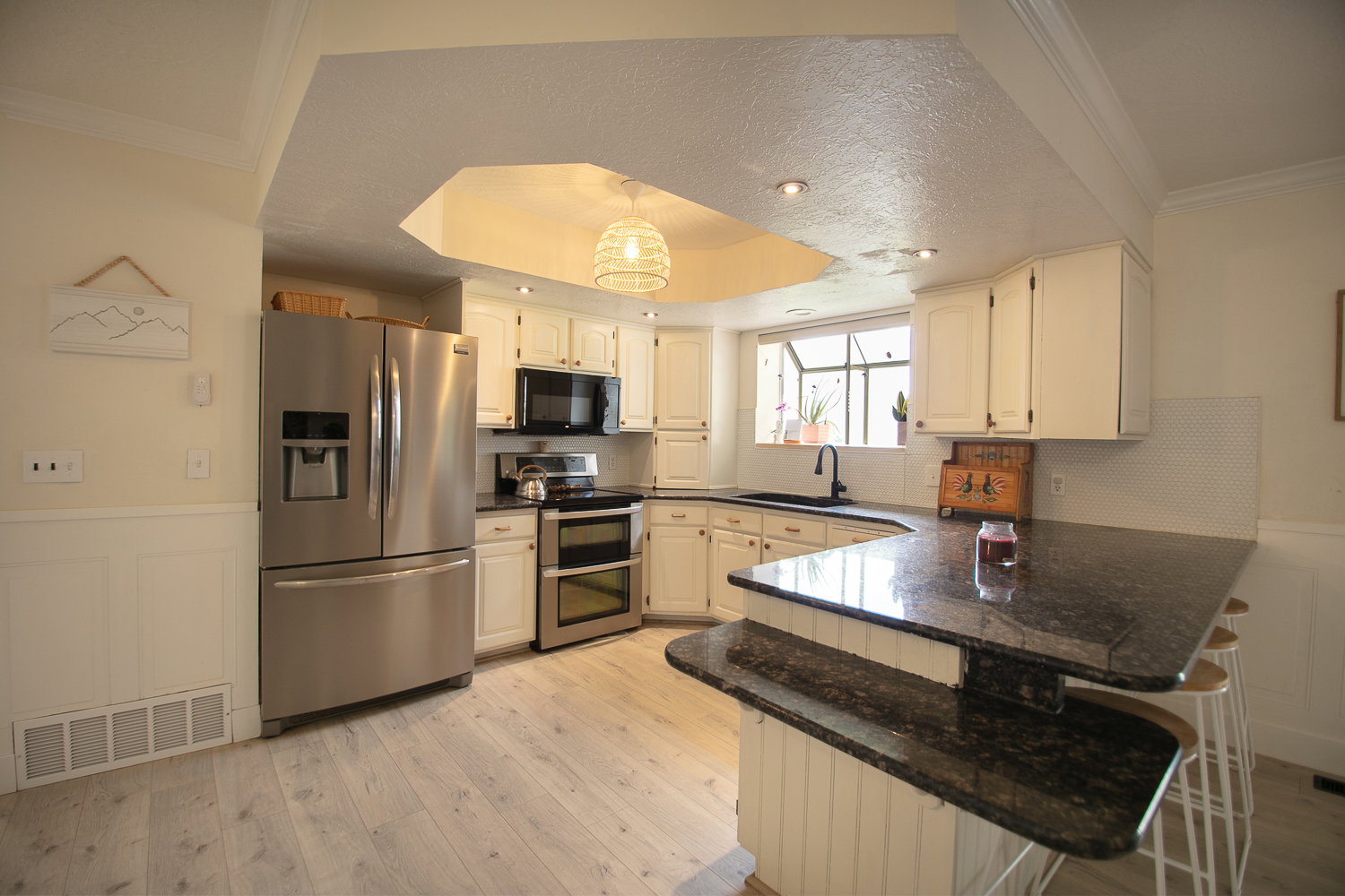 Kitchen featuring white cabinetry, stainless steel appliances, dark granite countertops, and light wood-finish flooring