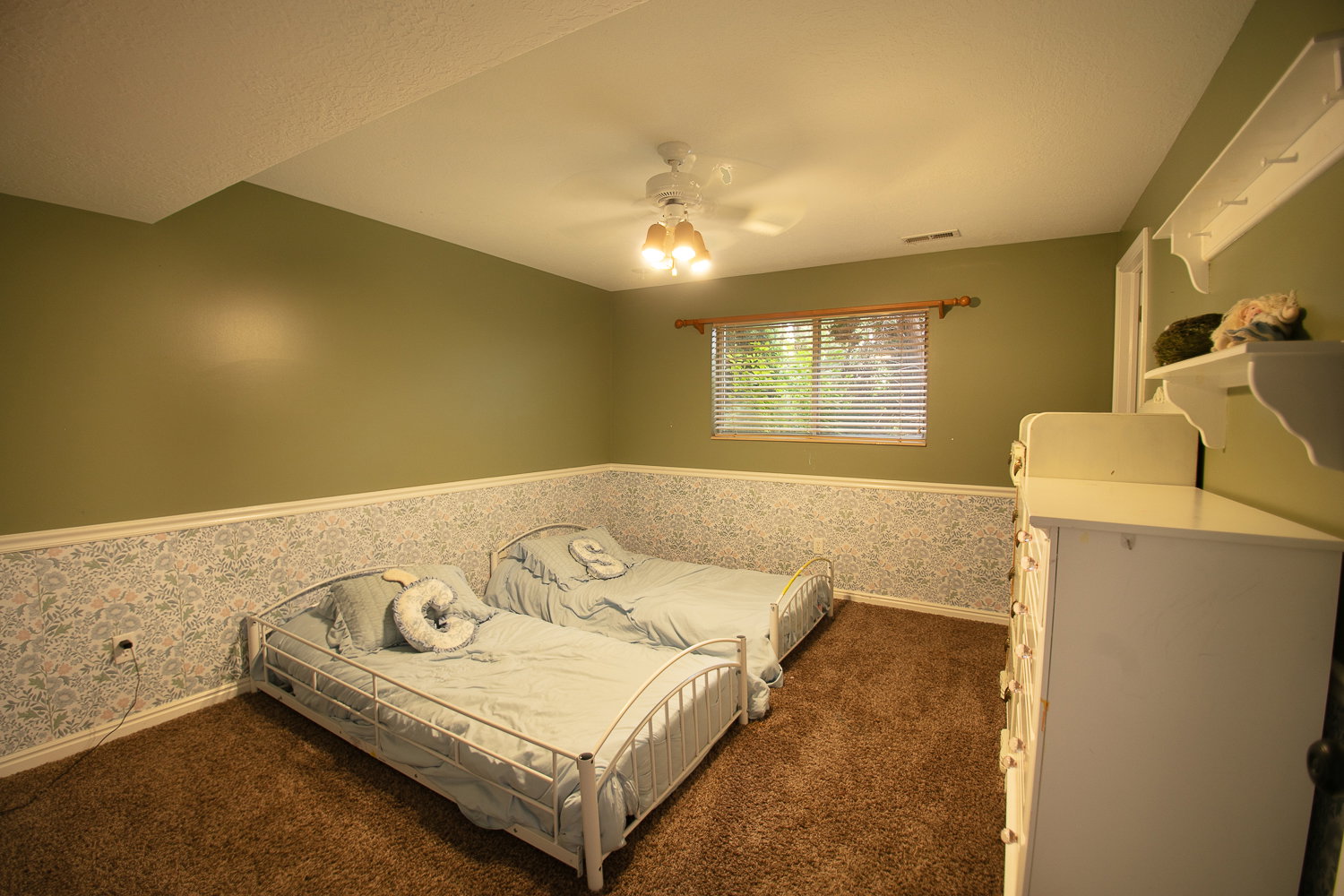 Carpeted room with a ceiling fan light fixture, a window featuring blinds, and walls with a patterned wainscoting
