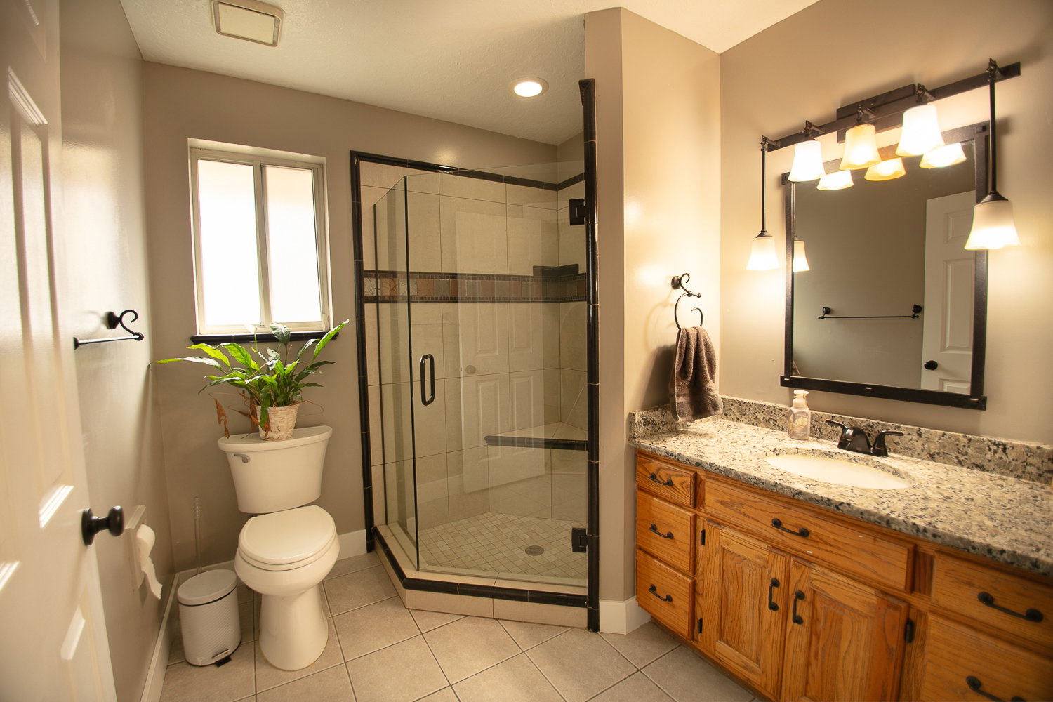 Bathroom featuring a corner glass-enclosed shower, light wood-finish vanity with granite-style countertop, integrated sink, and an overhead vanity light fixture