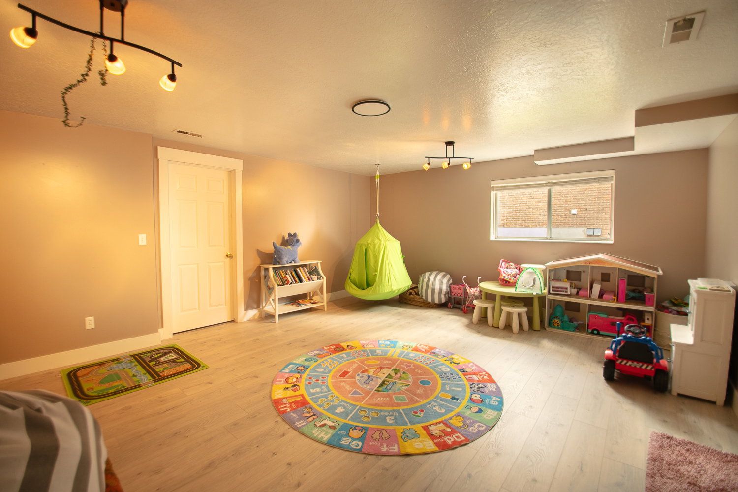 Expansive room featuring wood-finish flooring, a contemporary light fixture, a white paneled door, and a horizontal window with blinds