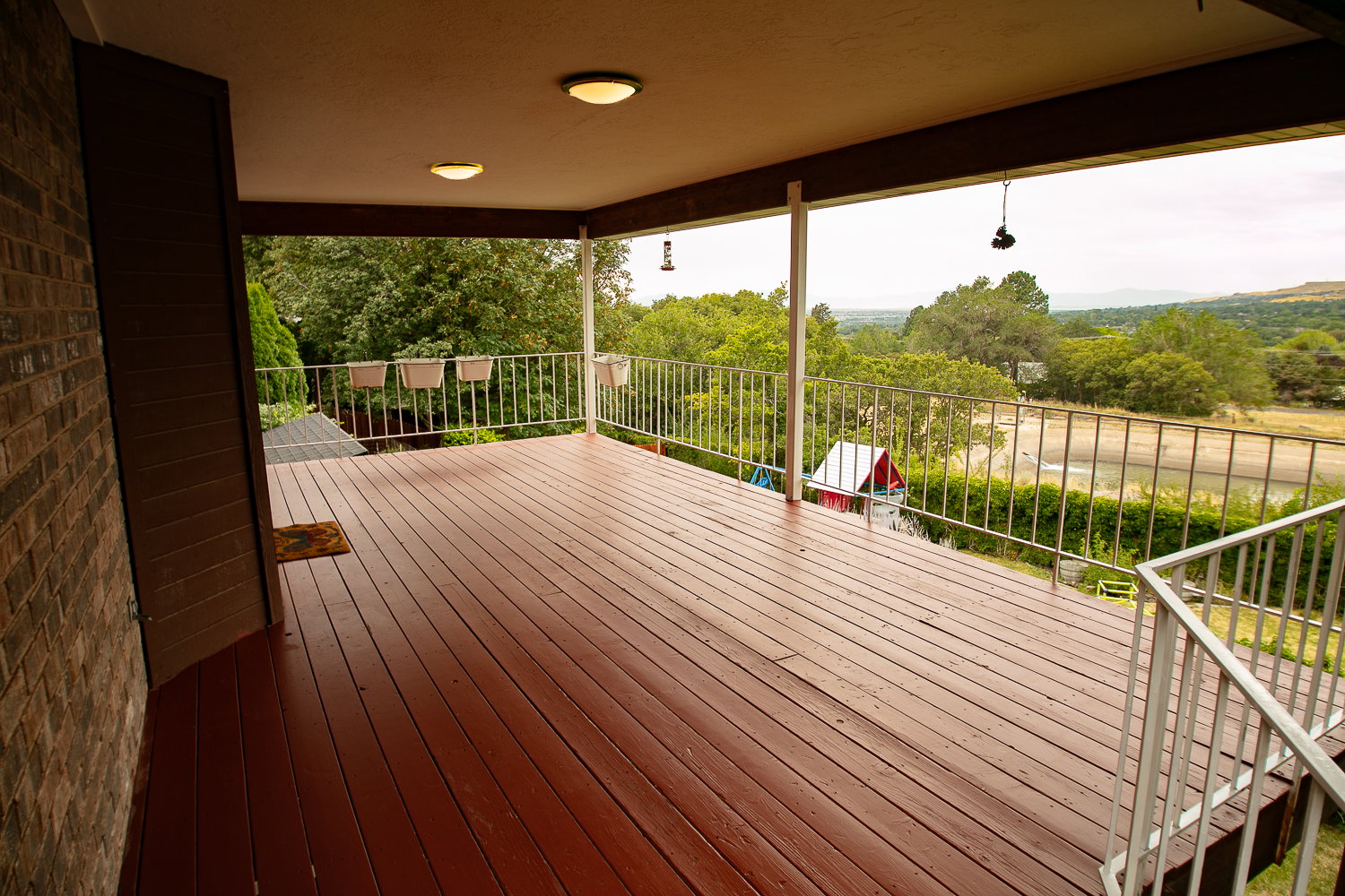 Expansive covered deck featuring rich wood-finish flooring, white metal railings, and dual overhead lighting fixtures