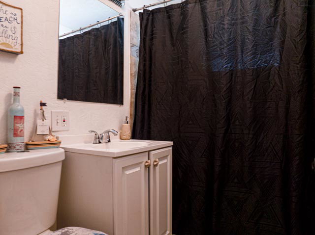 Bathroom featuring a white toilet, white vanity with integrated sink, chrome faucet, wall mirror, and a black shower curtain
