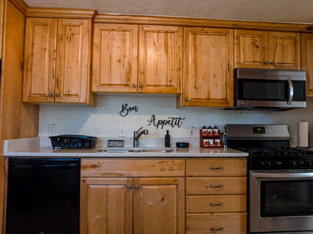 Kitchen featuring light wood cabinetry, a stainless steel microwave, a built-in dishwasher, a stainless steel range with gas cooktop, and a light-toned countertop