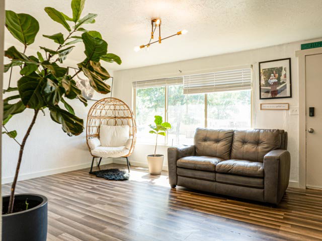 Living area featuring wood-finish flooring, white walls, and a large window with horizontal blinds