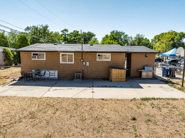 Rear exterior with a concrete patio, brown siding, and a dark shingled roof
