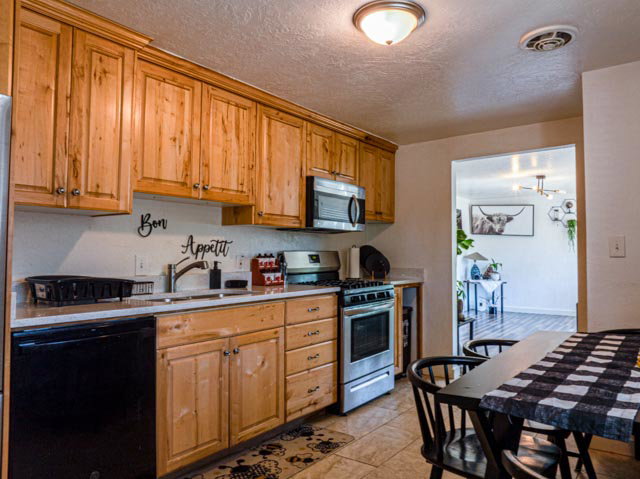 Kitchen featuring wood cabinetry, stainless steel range, built-in microwave, black dishwasher, and a light-toned countertop