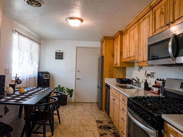 Kitchen featuring warm wood cabinetry, light-toned countertops, a stainless steel microwave, and a black gas range
