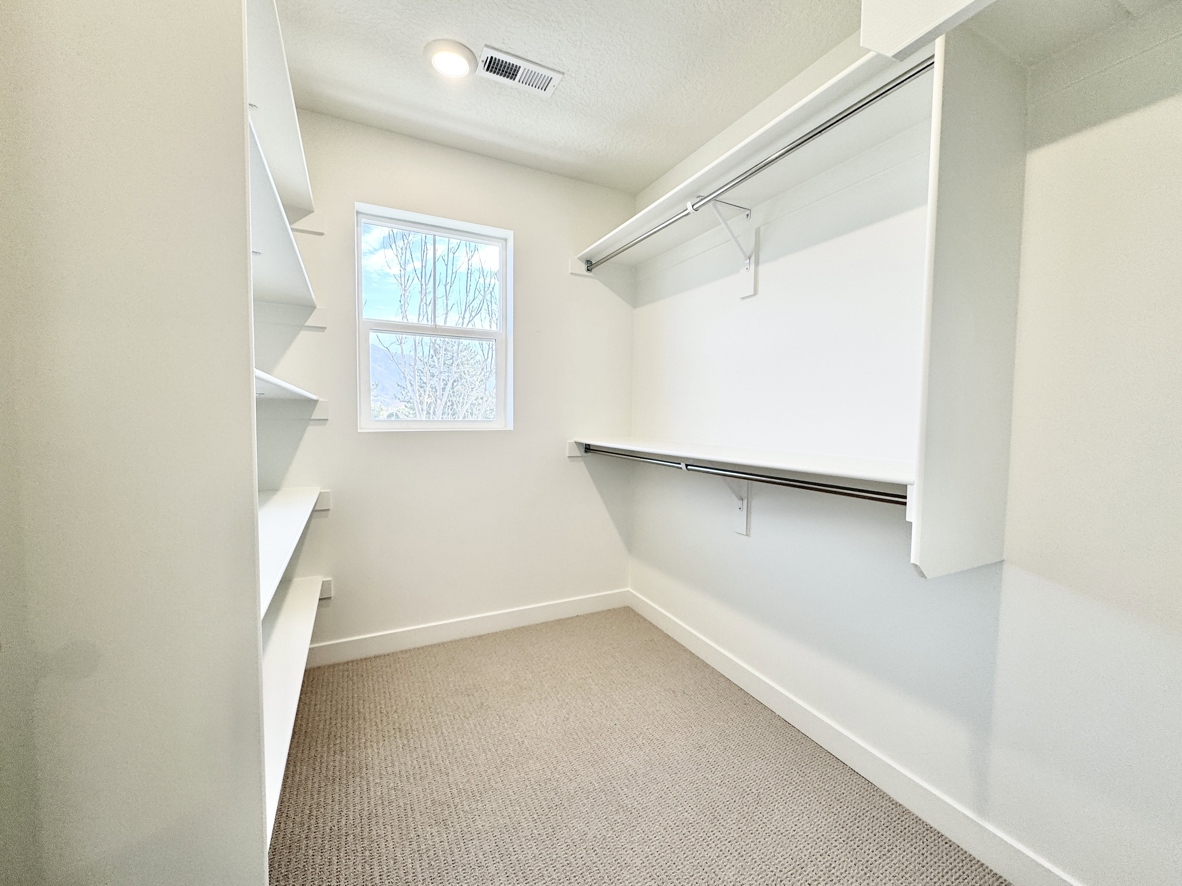 Walk-in closet with built-in shelving, dual hanging rods, and a window for natural light