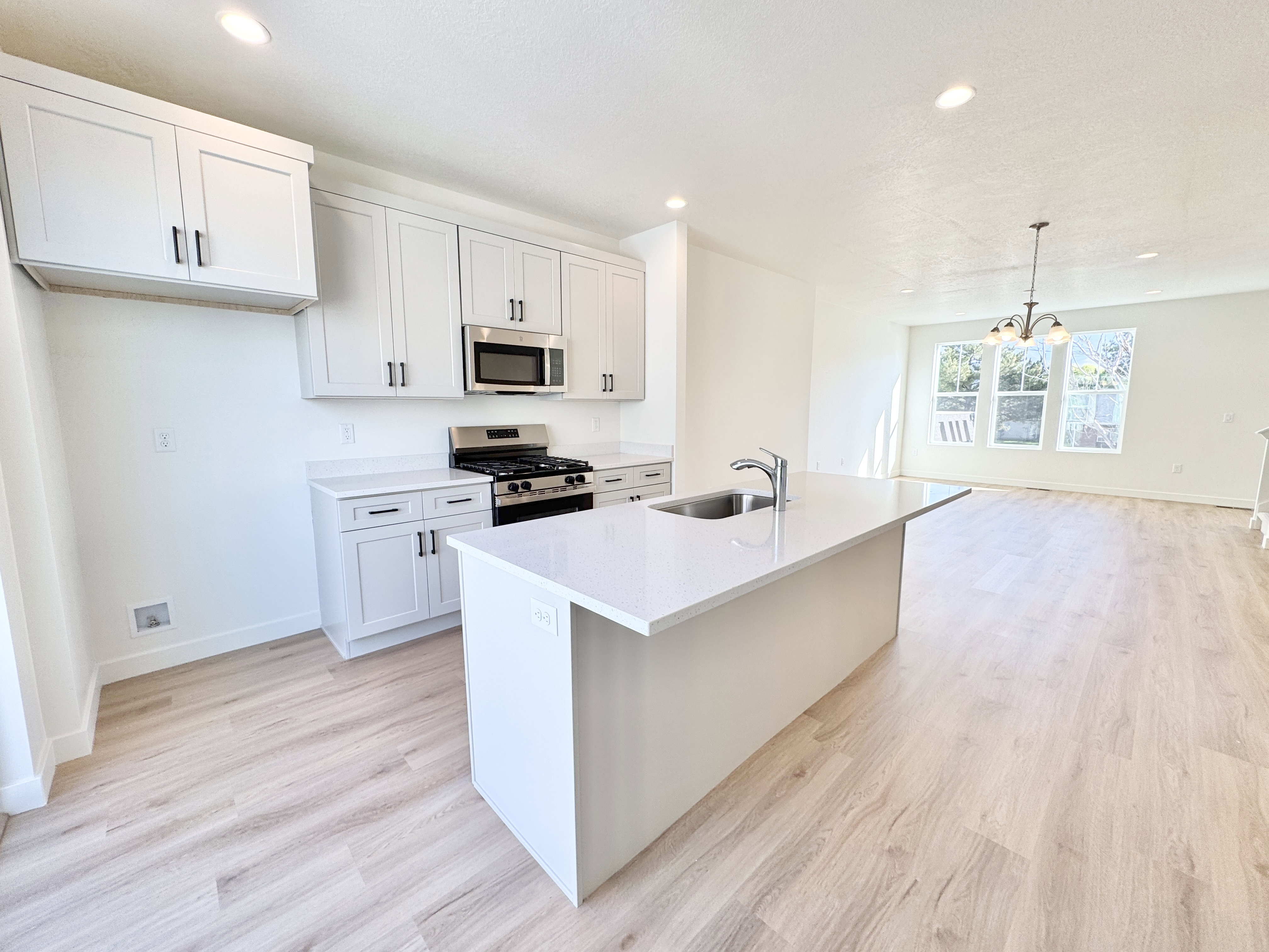 Modern kitchen featuring light wood-finish flooring, white cabinetry with dark hardware, stainless steel appliances, a center island with integrated sink, and recessed lighting