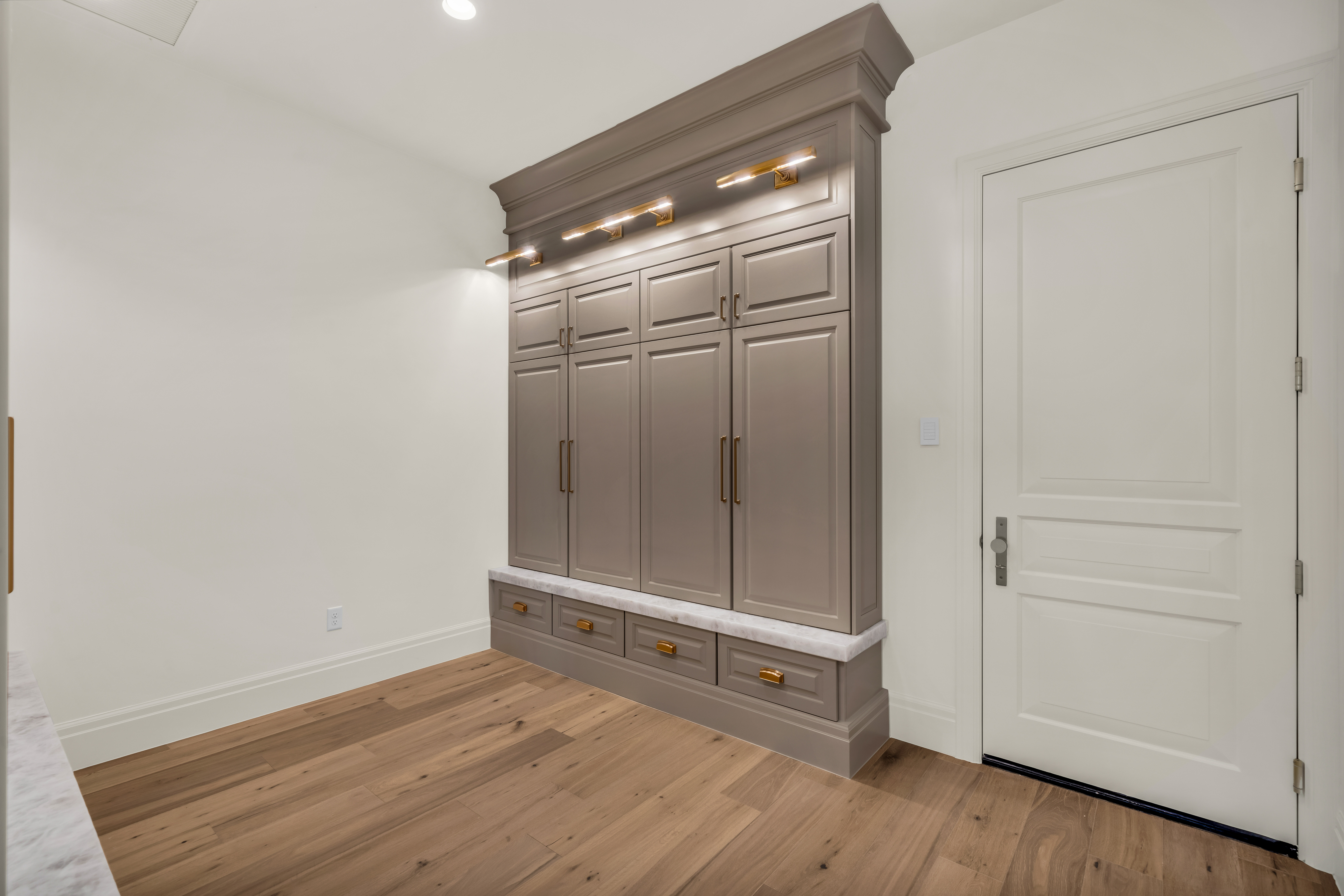Built-in cabinetry with ample storage, integrated lighting, a marble-look countertop, brass hardware, and wood-finish flooring