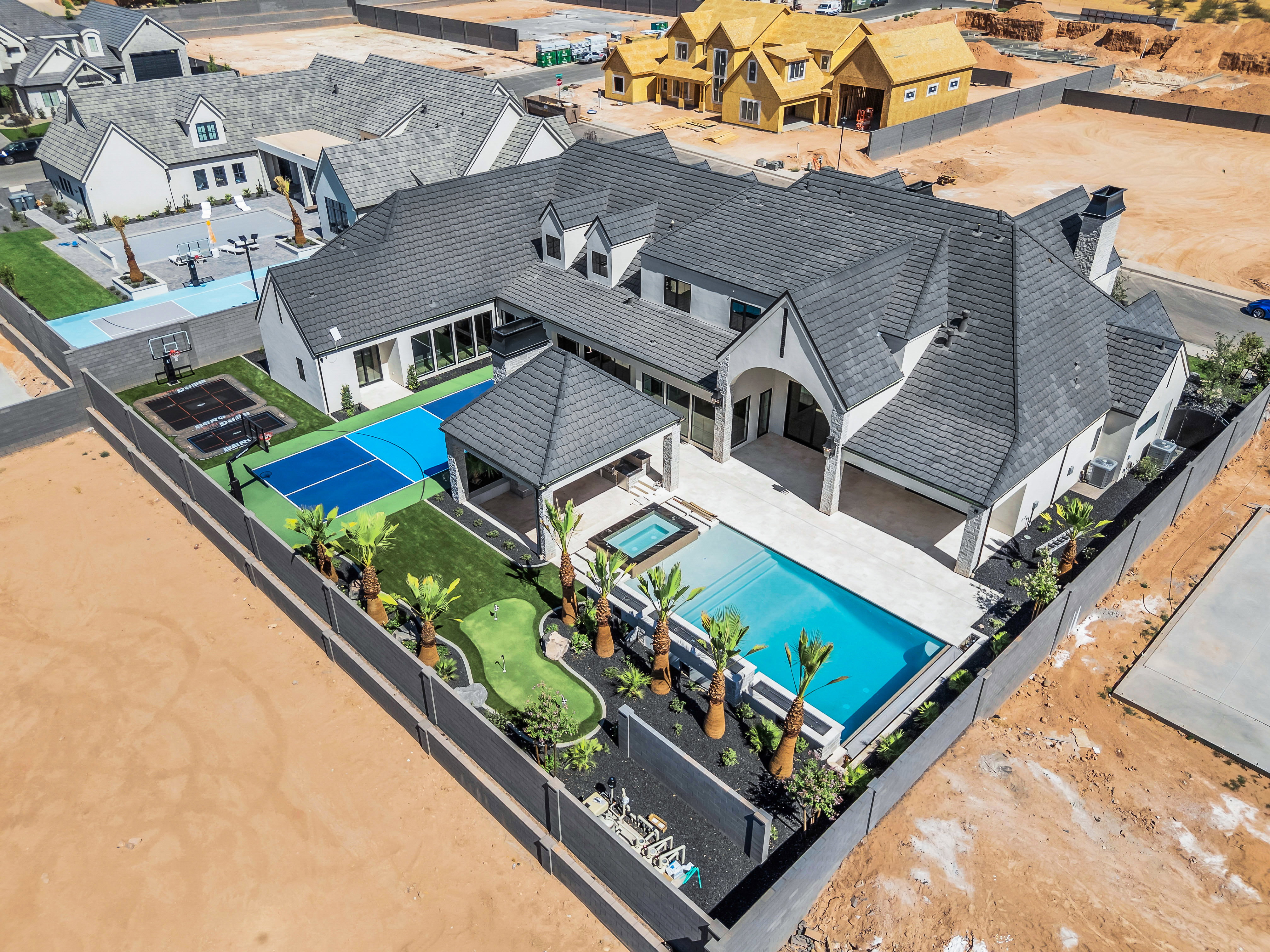 Expansive backyard oasis featuring a swimming pool, integrated spa, covered patio, sport court, putting green, and mature palm trees