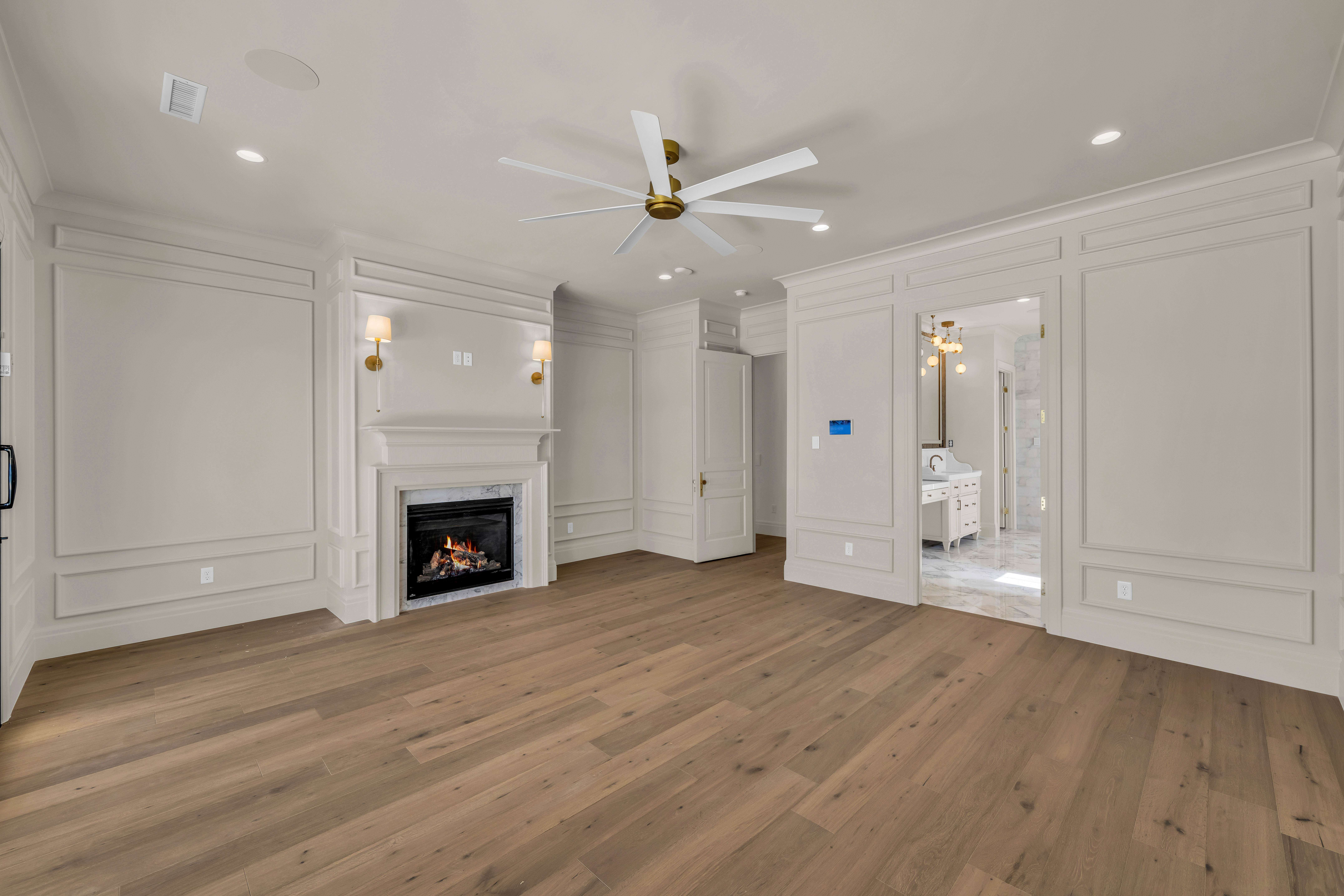 Spacious room featuring wood-finish flooring, an ornate fireplace with sconce lighting, extensive wall paneling, and a ceiling fan