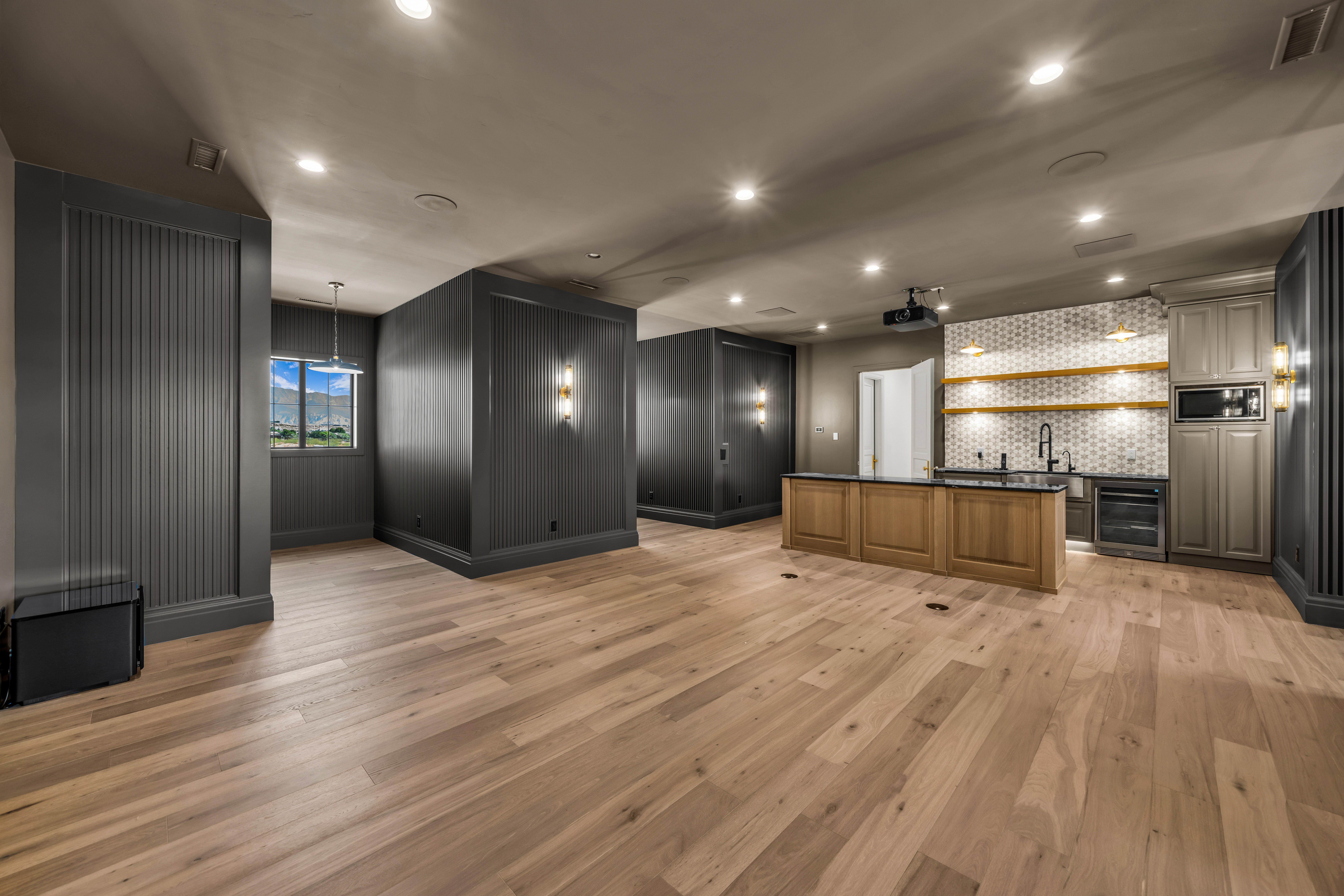 Spacious room featuring wood-finish flooring, recessed lighting, and dark gray accent walls with paneling
